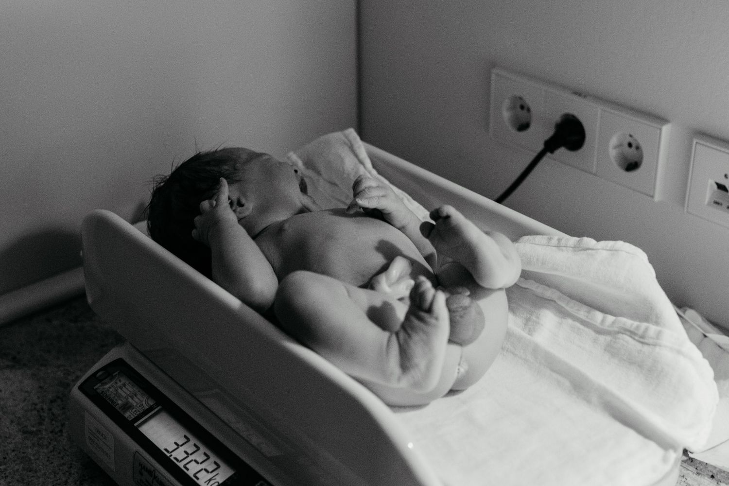 A black-and-white image of a newborn being weighed after birth in Orange County.