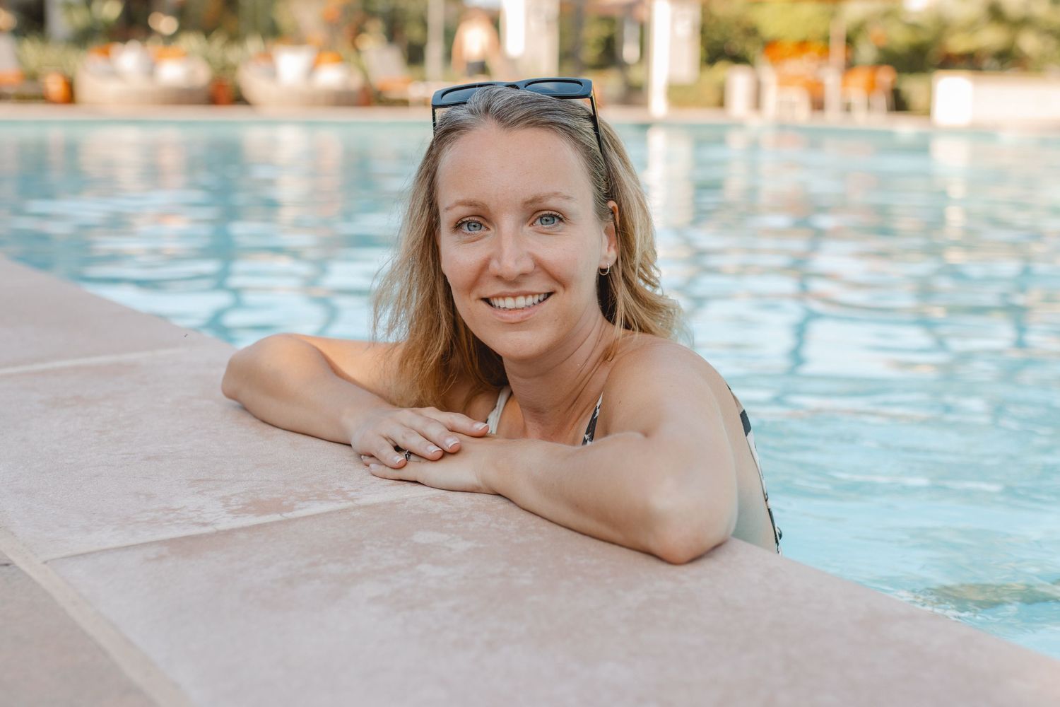 Person relaxing at the edge of a swimming pool with crystal clear blue water on a sunny day in Laguna Beach.