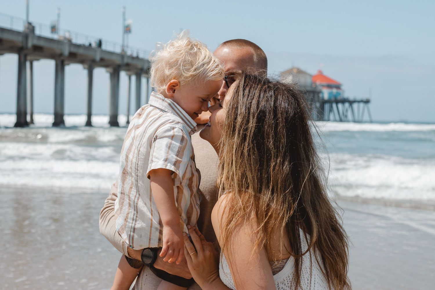 Young family embraces tenderly on a sandy beach as gentle waves roll in behind them in Laguna Beach.