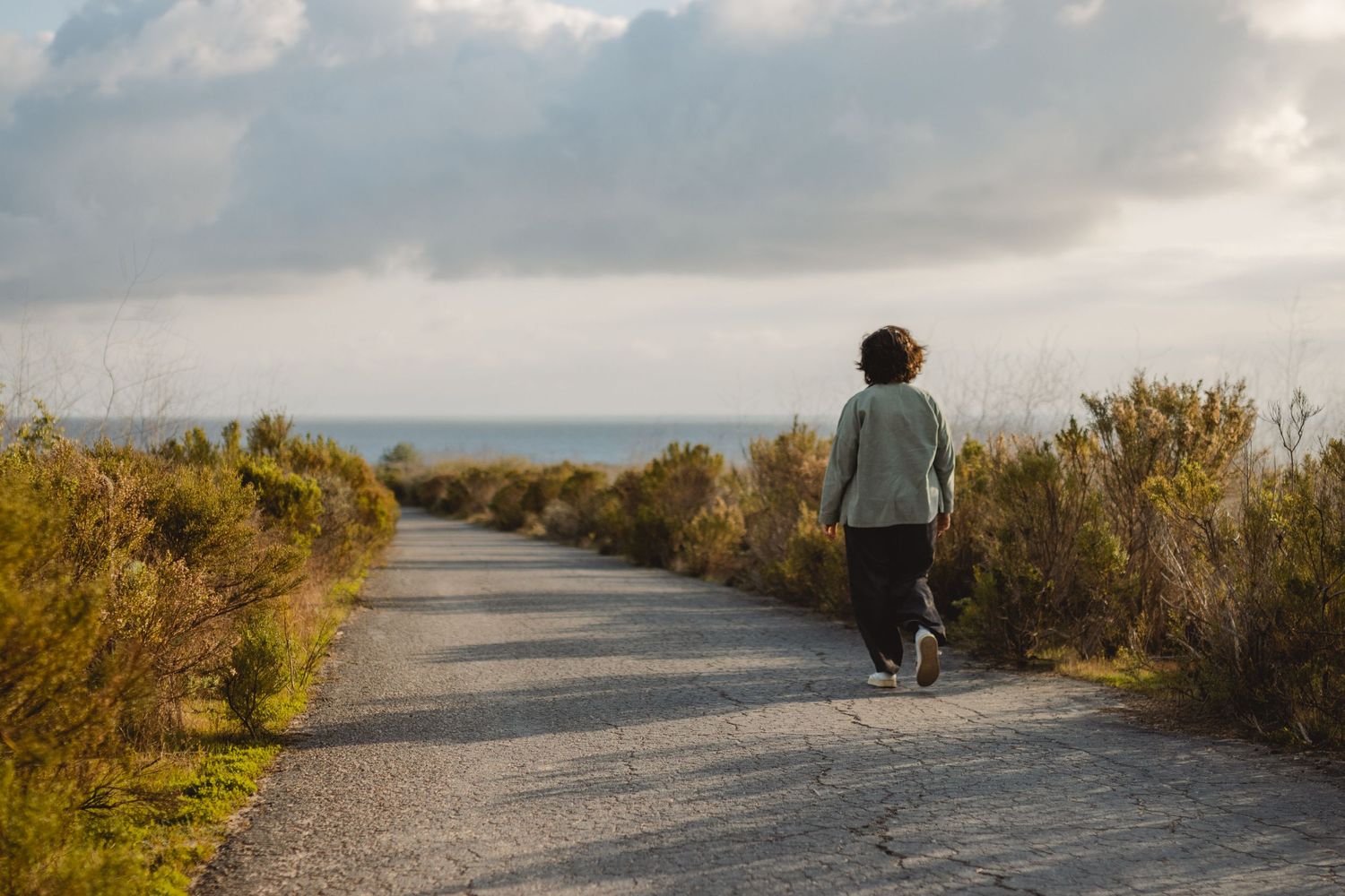 A scenic gravel pathway winds through coastal shrubland on a cloudy autumn day near the ocean in Orange County.