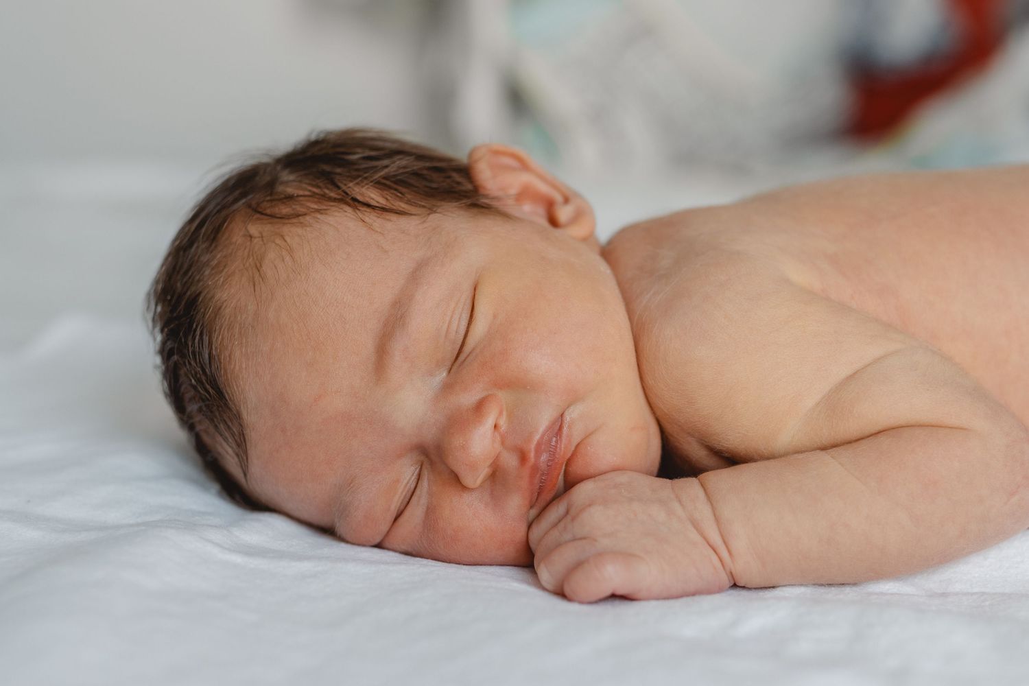 Sleeping newborn lying on a soft white blanket in Laguna Beach with eyes closed and peaceful expression in peaceful slumber.