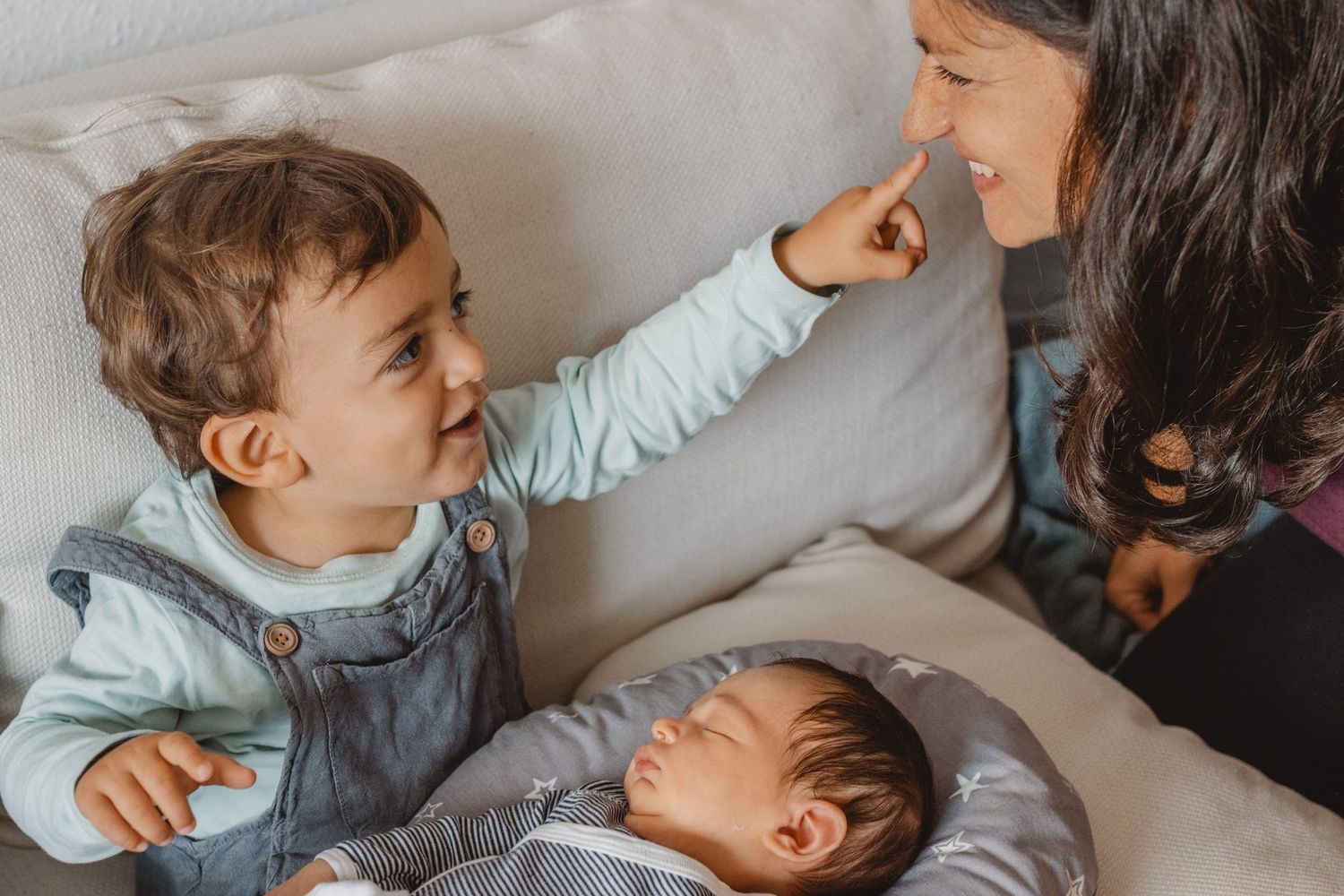 Happy toddler and newborn laughing and playing together on a cozy gray sofa during candid family moments in Newport Beach.