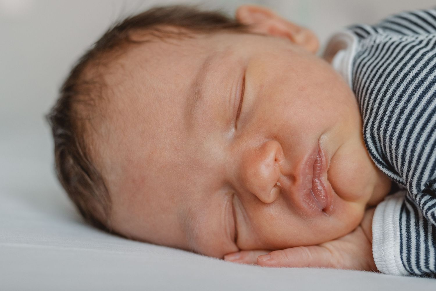A sleeping newborn baby in a striped onesie rests peacefully in a sequence of close-up shots at Huntington Beach.
