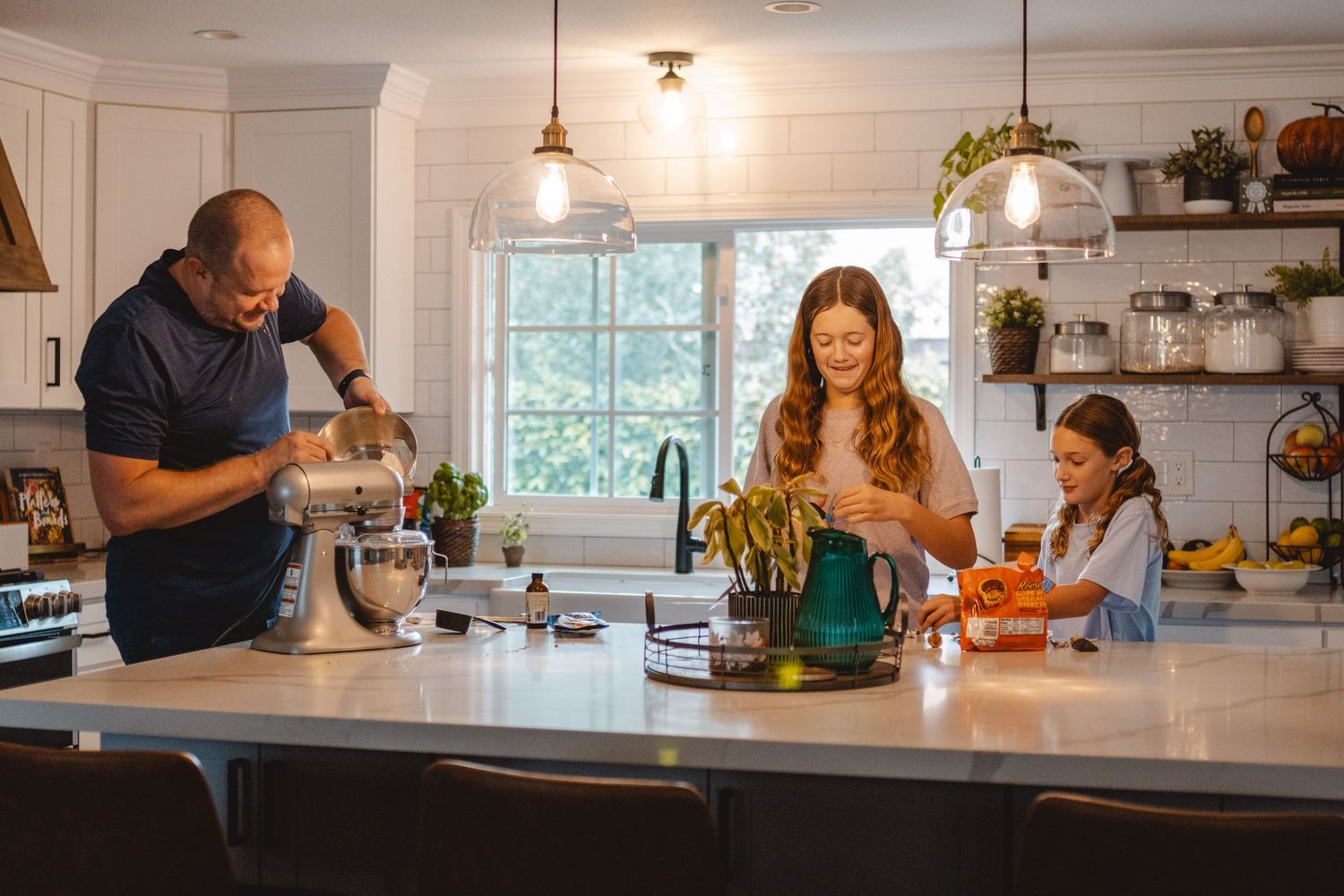 Family members preparing food together in a bright modern kitchen with white cabinets and floating shelves in Laguna Beach.