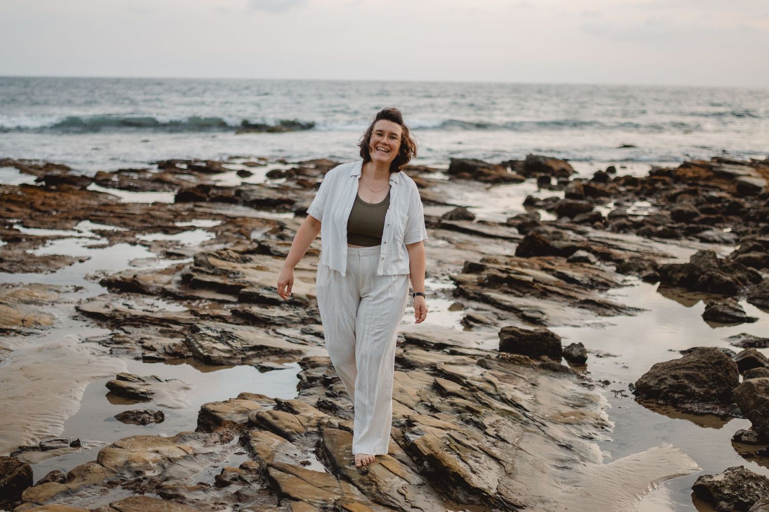 Rocky coastal beach landscape with person walking along rugged shoreline during overcast day at sunset in Long Beach.