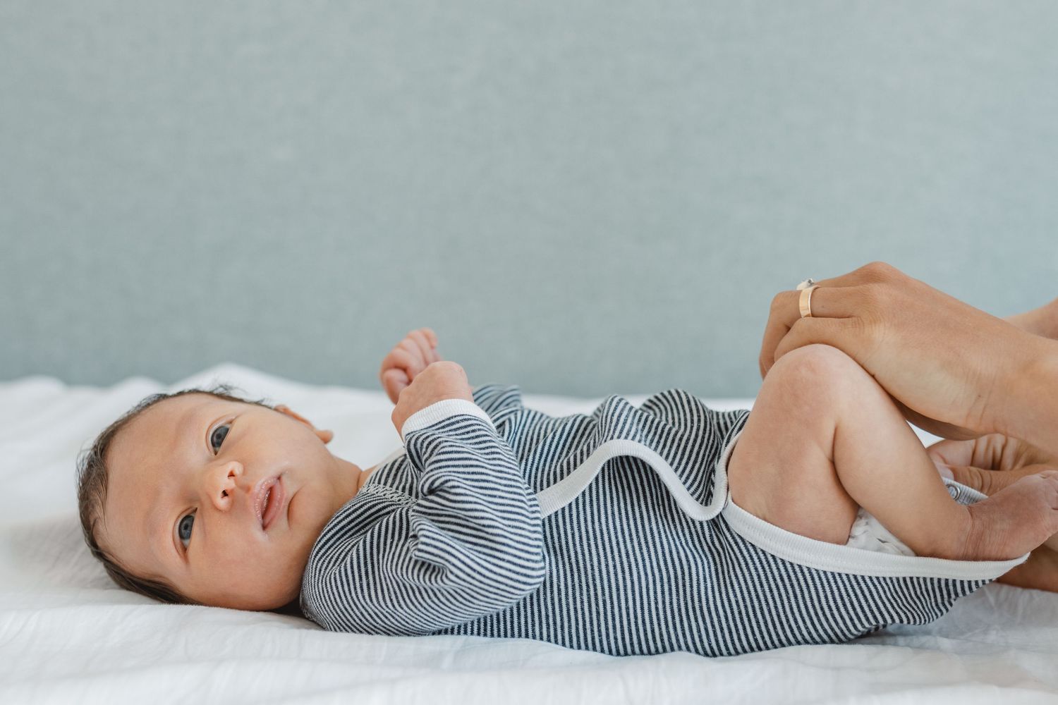 Baby lying on soft gray surface wearing striped bodysuit in horizontal progression of poses in Huntington Beach.
