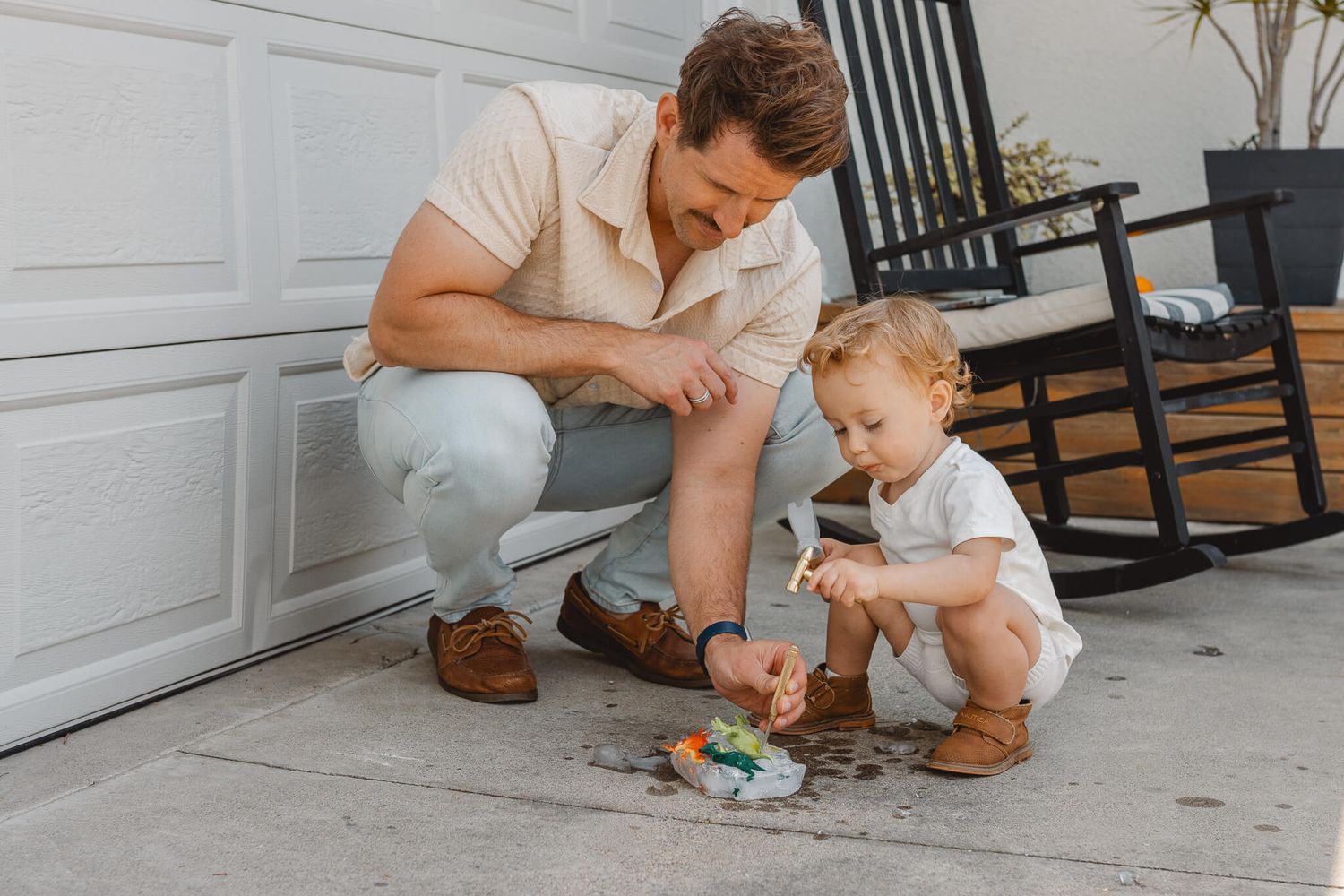 Adult and child in casual clothing squat together on a porch playing with small toys.