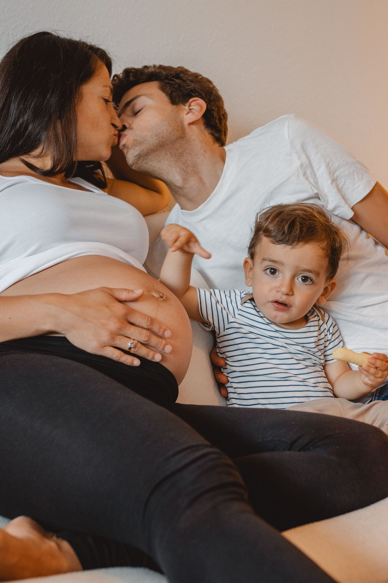 A loving family cuddles together on a cream-colored couch in Laguna Beach while wearing a striped shirt and black pants.