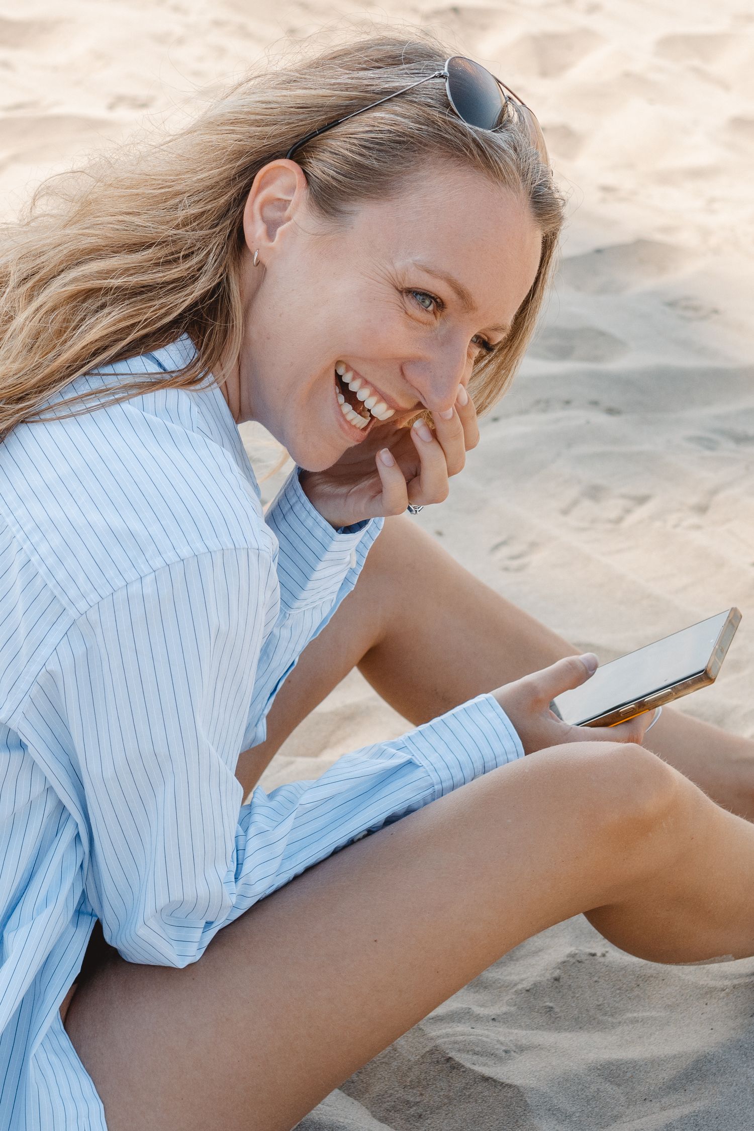 Person in striped shirt lying on sand at beach looking at mobile phone with joyful expression in Laguna Beach.