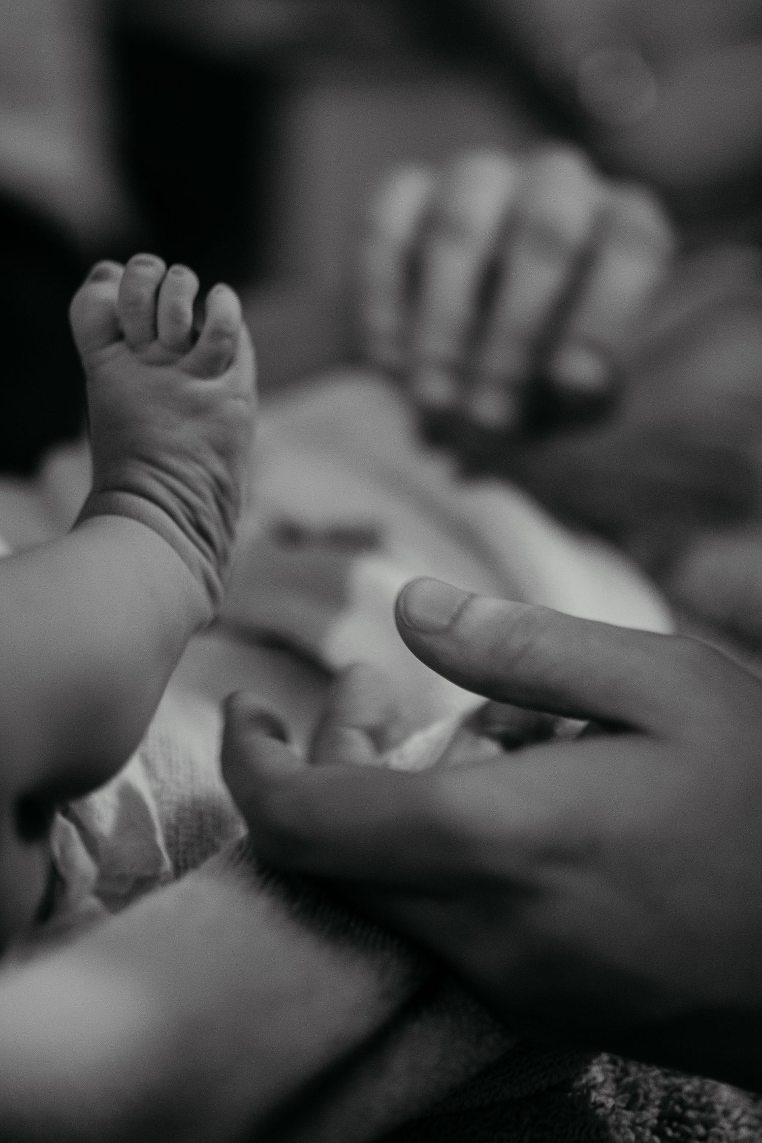 Black and white image of hands and newborn feet reaching out and connecting together, symbolizing unity and support in Newport Beach.