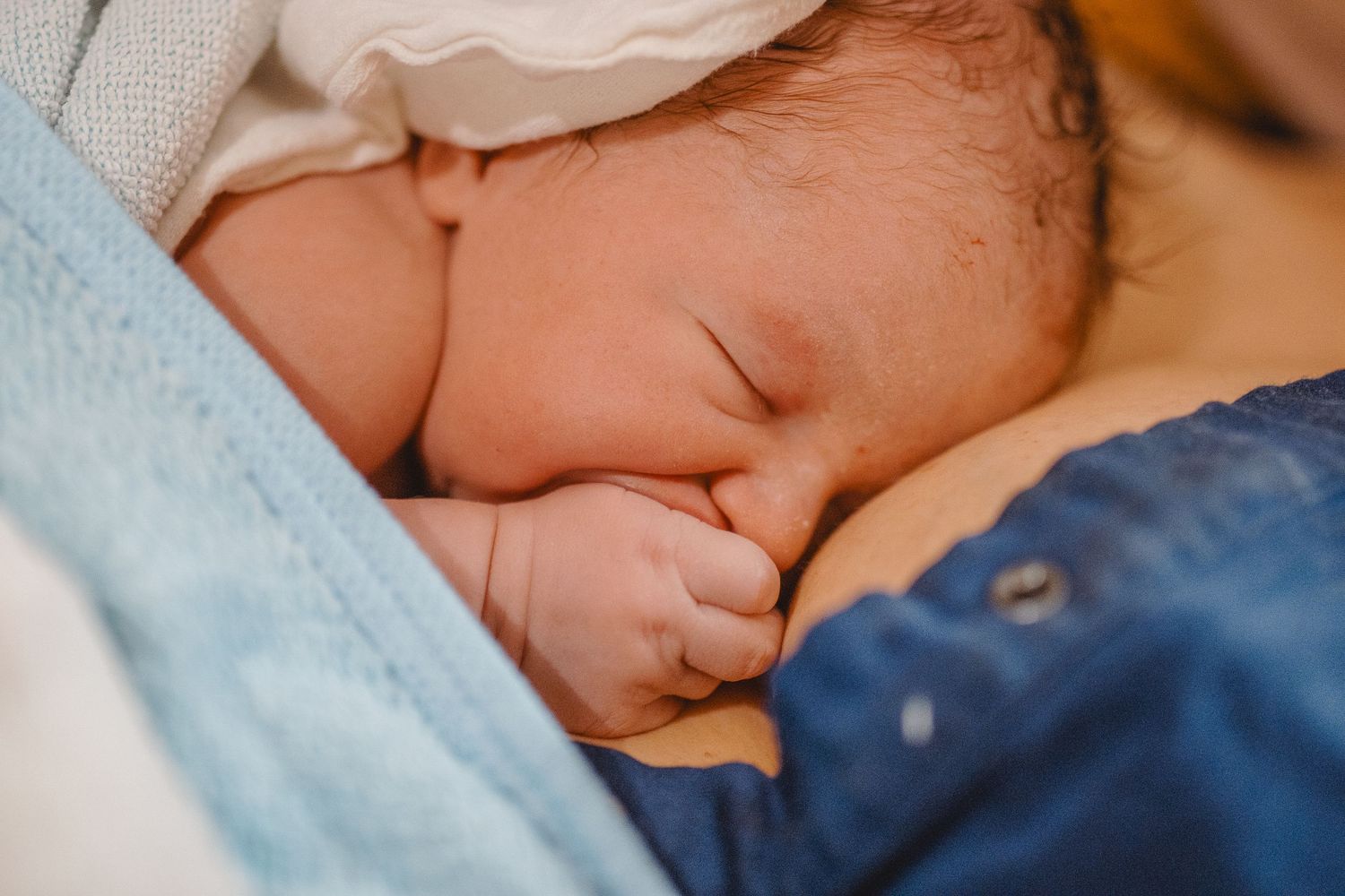 A few minutes old newborn lies sleeping with its thumb in its mouth on the mother’s chest in Huntington Beach.