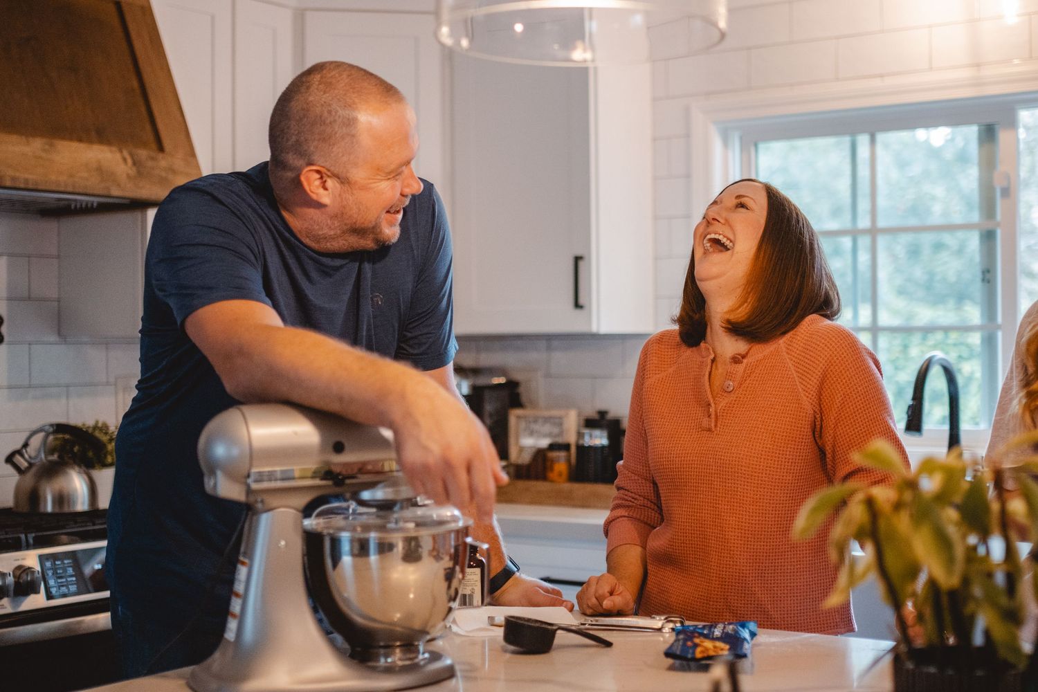 Two people laugh together while cooking and pouring ingredients in a bright modern kitchen in Newport Beach.