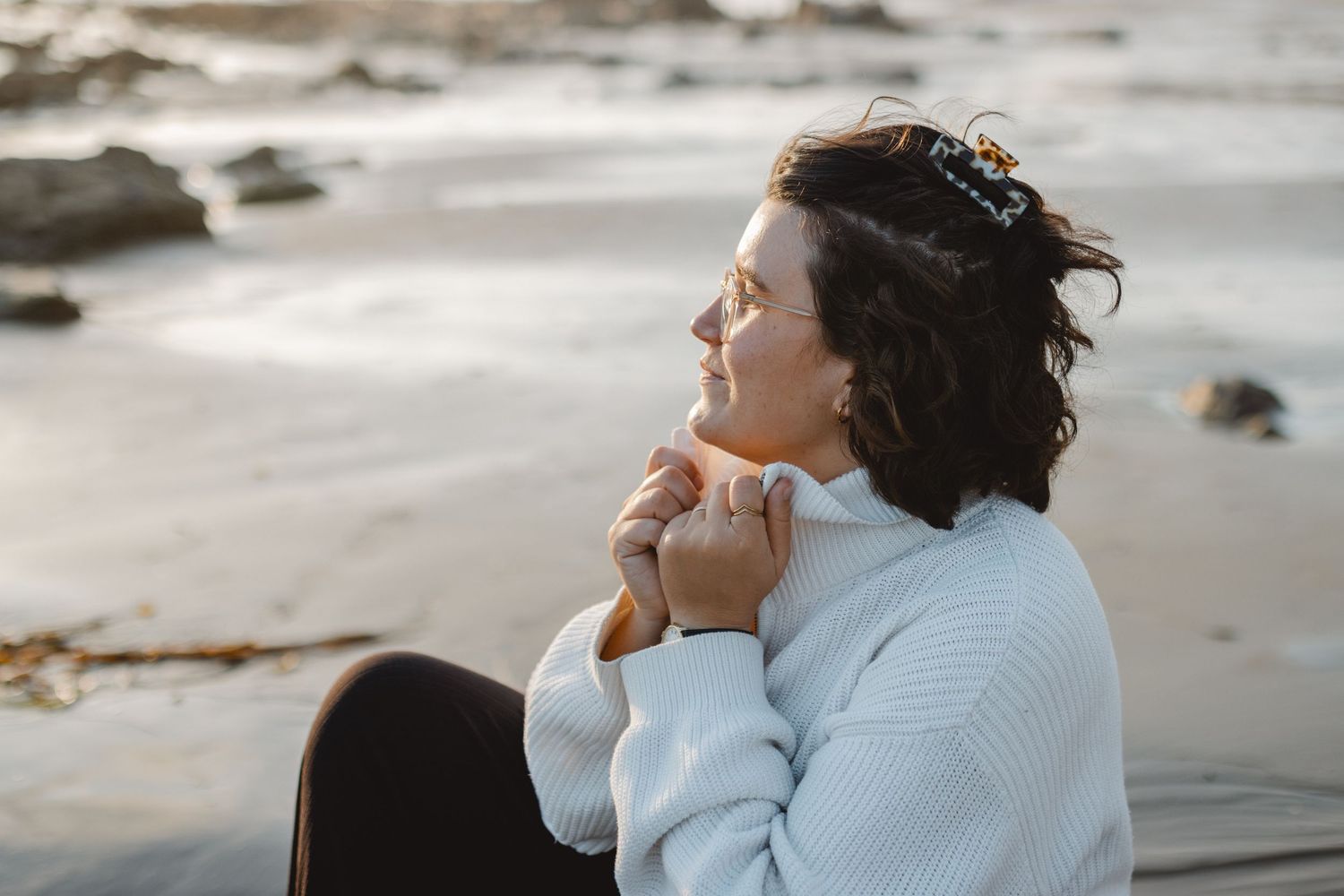 Person in light blue sweater enjoying peaceful moment at beach during sunset in Newport Beach.