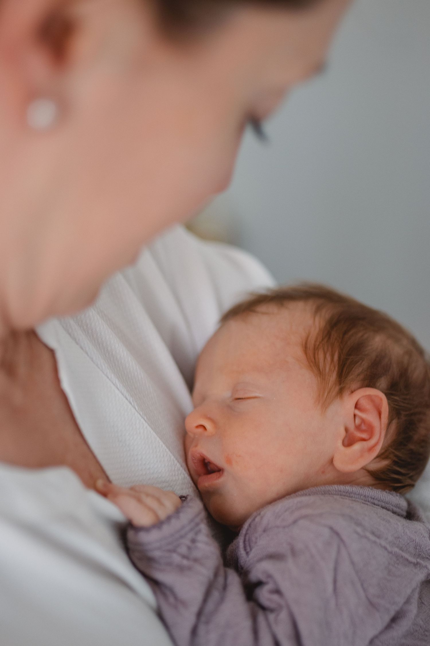 A sleeping baby in a gray onesie rests peacefully against someone wearing a white sweater in Huntington Beach.