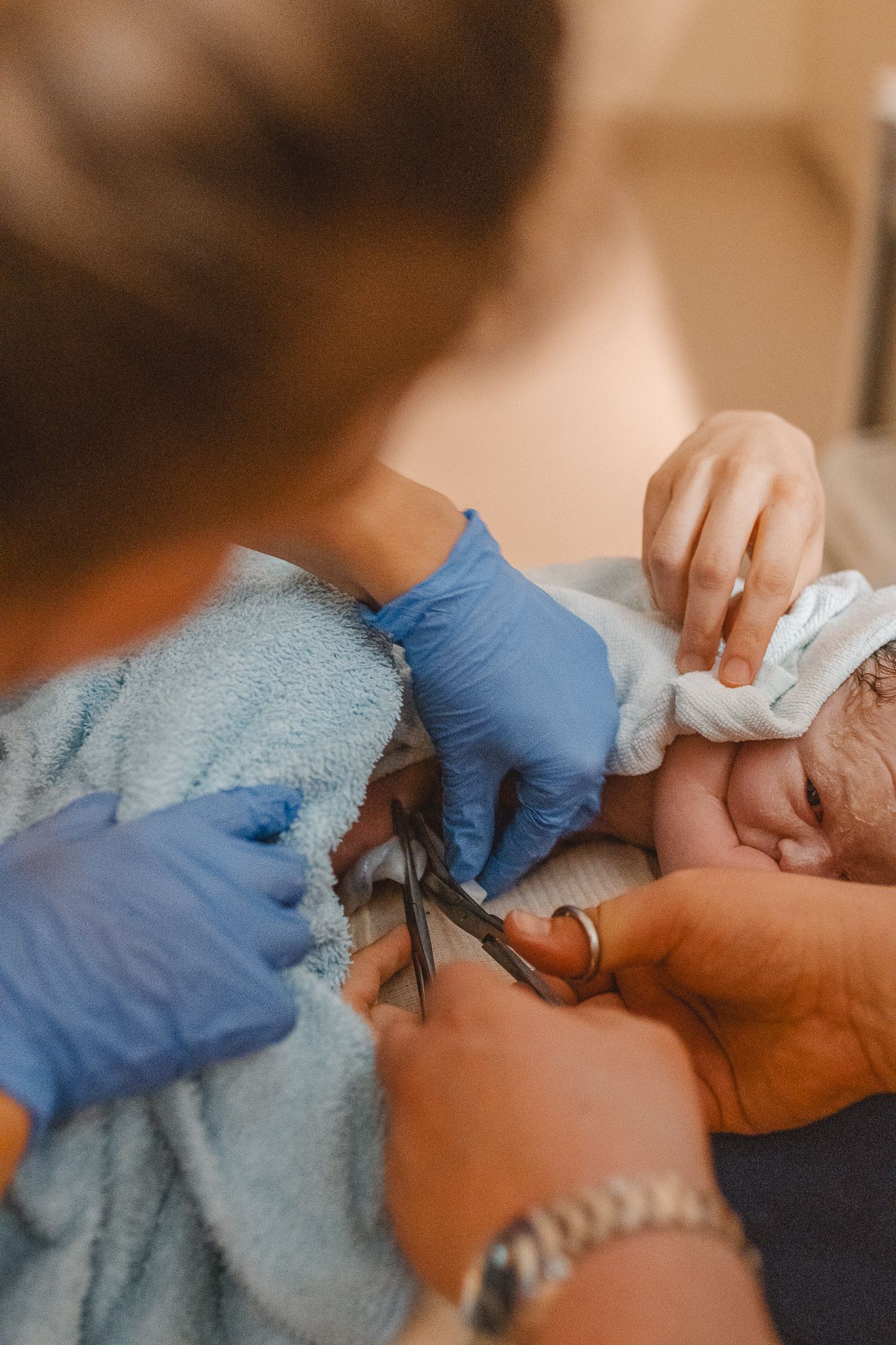 Healthcare worker wearing blue gloves and another person cuts the umbilical cord of a newborn in Newport Beach.