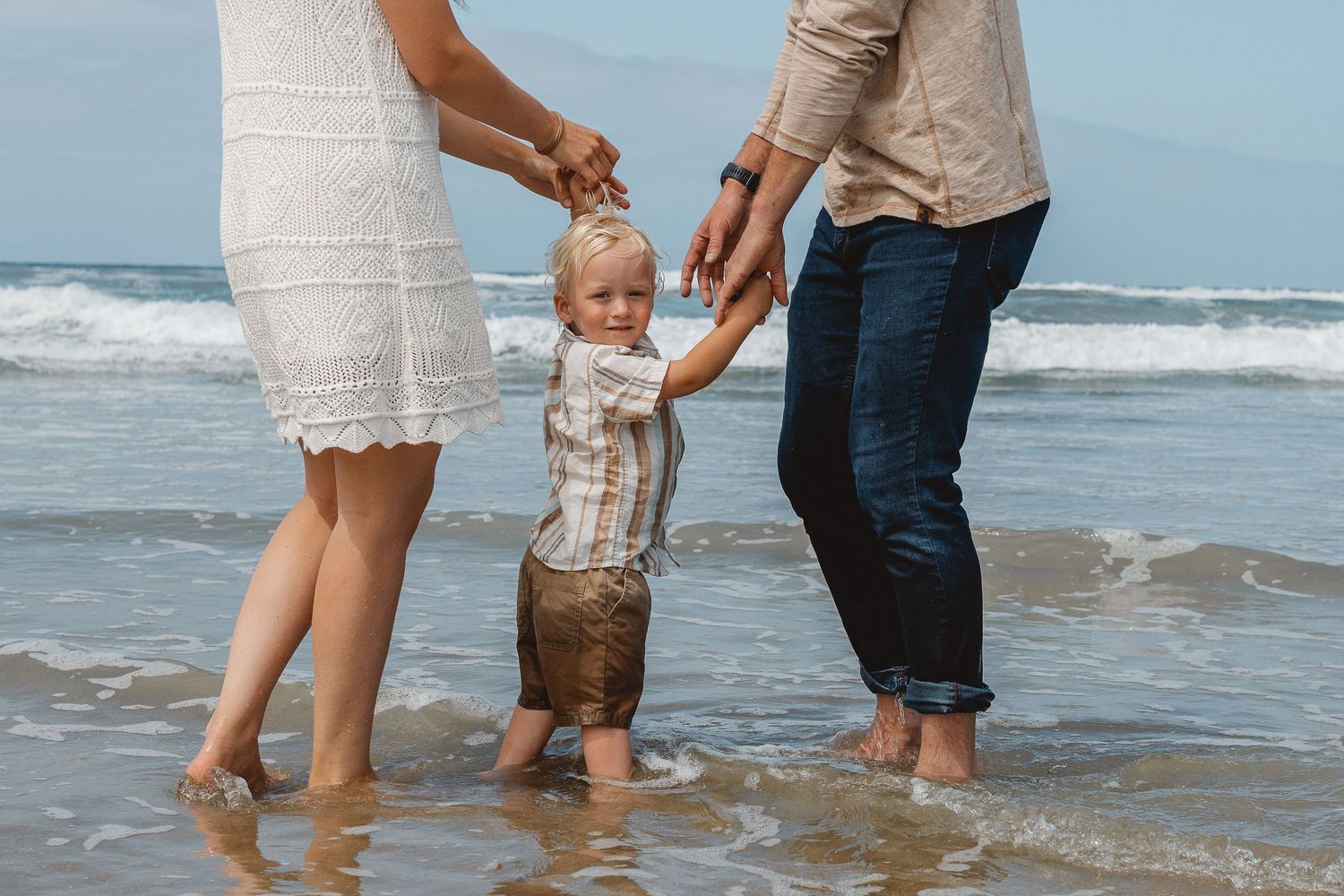Family standing on a sunny beach by the ocean's edge where waves meet sand in Huntington Beach.