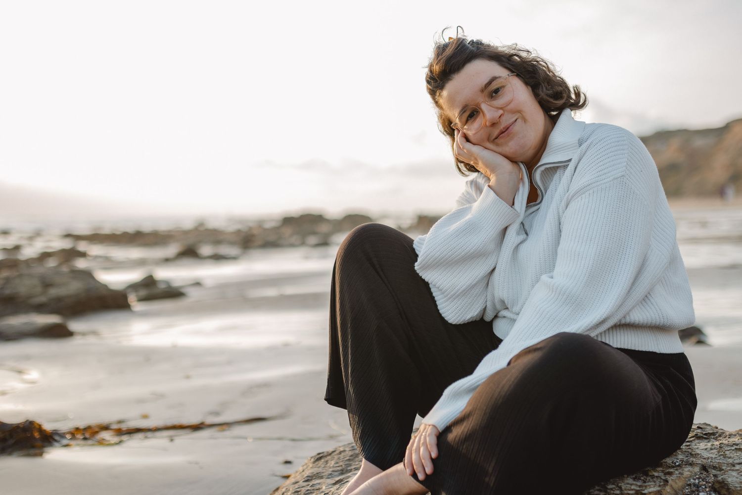 A serene set of beach photoshoot images with rocky coastline and crashing waves in the background during sunset in Laguna Beach.