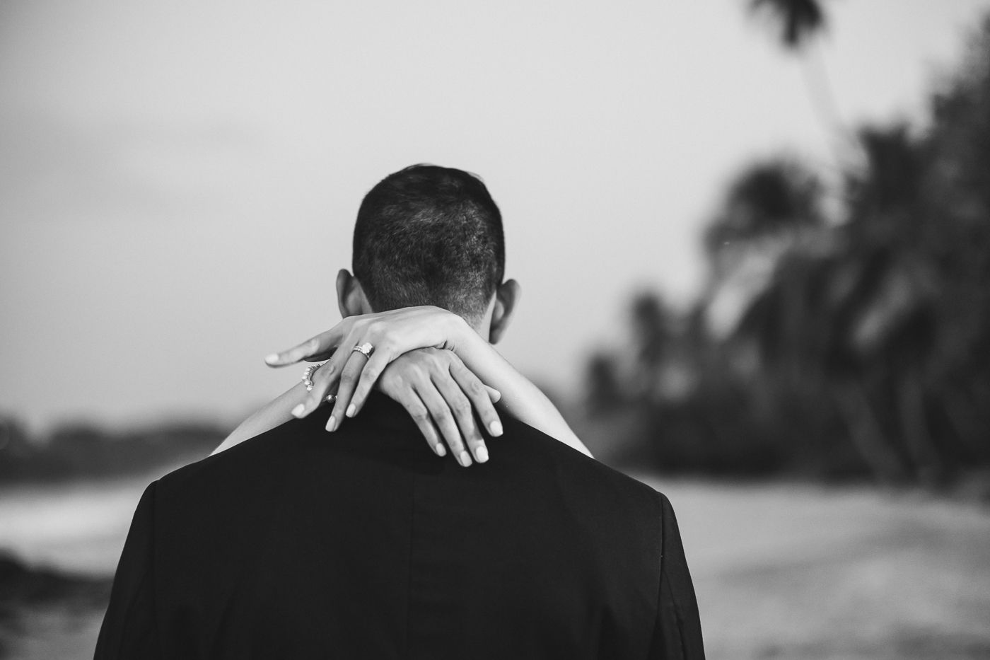 Black and white photo of a couple embracing on a beach, woman's hand resting on man's shoulder.