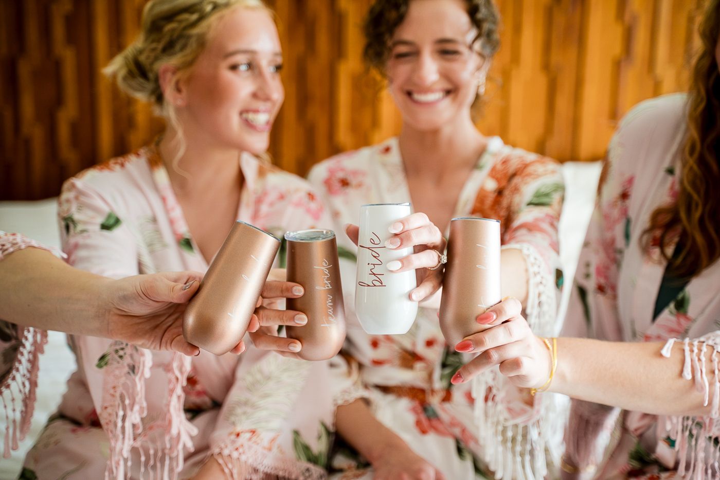 Several people in matching pink floral robes share drinks and laughter.