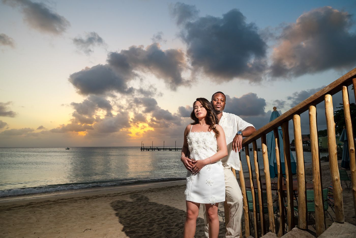 A couple poses for a romantic sunset photo on a beachfront deck with ocean views.