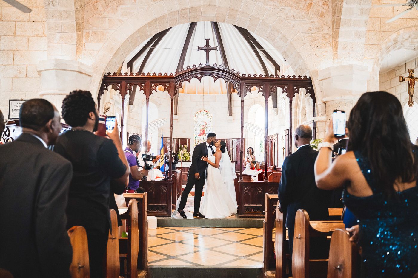 Wedding ceremony under domed church altar with guests seated in wooden pews.