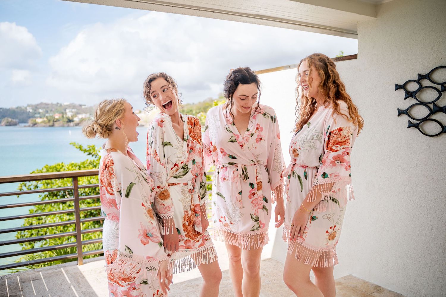 Friends in matching pink floral robes laugh together on a balcony overlooking the ocean in Saint Lucia, sandals resort