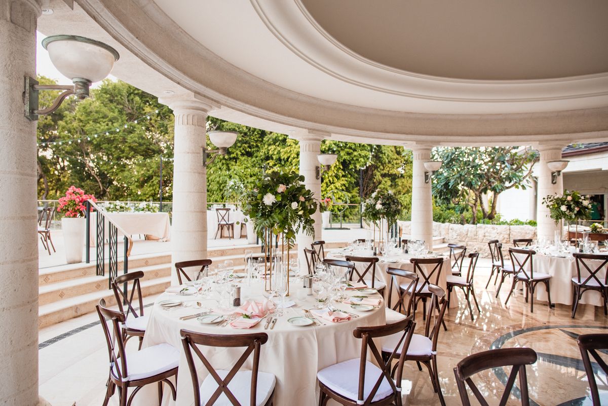 Elegant curved patio dining area with white columns, crossback chairs, and tables set for formal dining service. Sandy Lane barbados