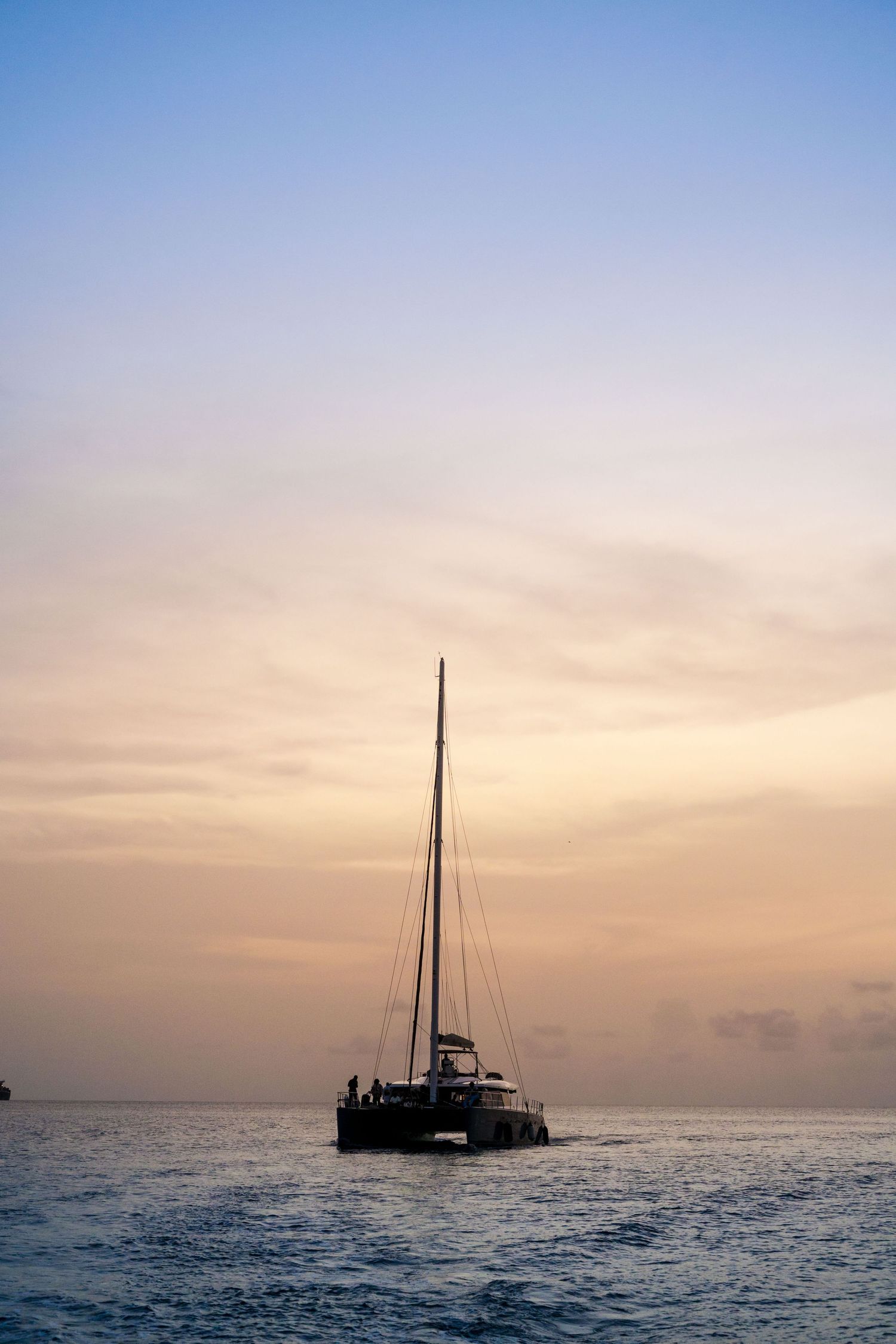 A barbados sunset seascape series showing silhouettes of sailboats on the horizon against a gradient sky over calm ocean waters.