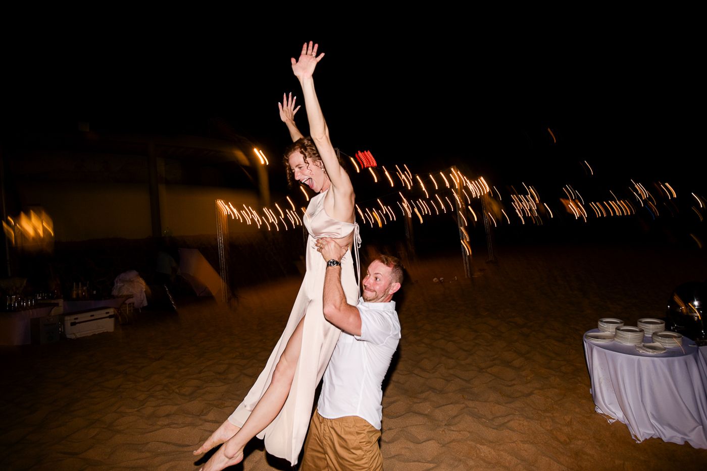 Wedding reception dance party on the beach with string lights creating a romantic atmosphere.