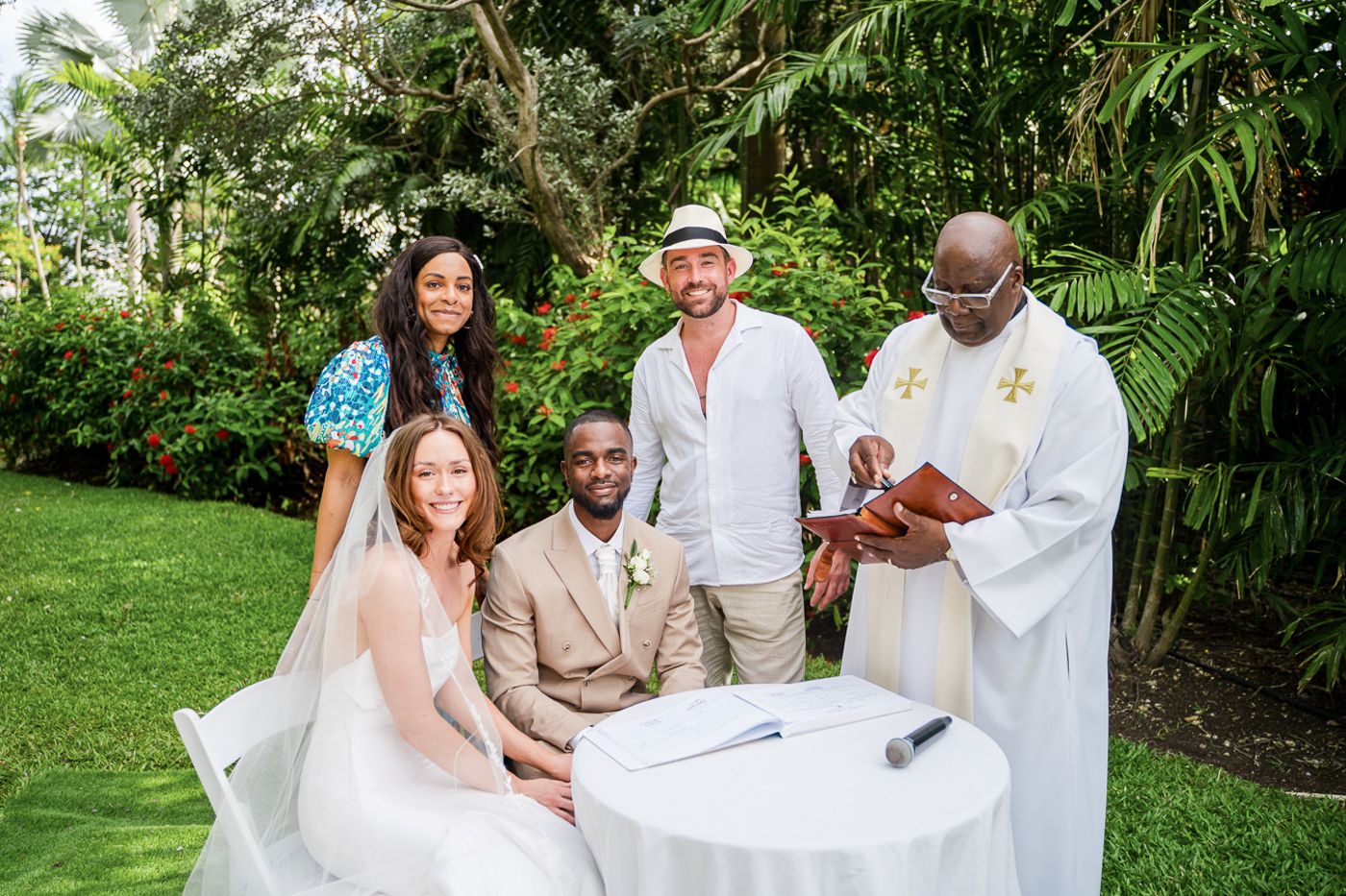 Guests celebrating during a joyful outdoor wedding ceremony with white draping and tropical greenery.