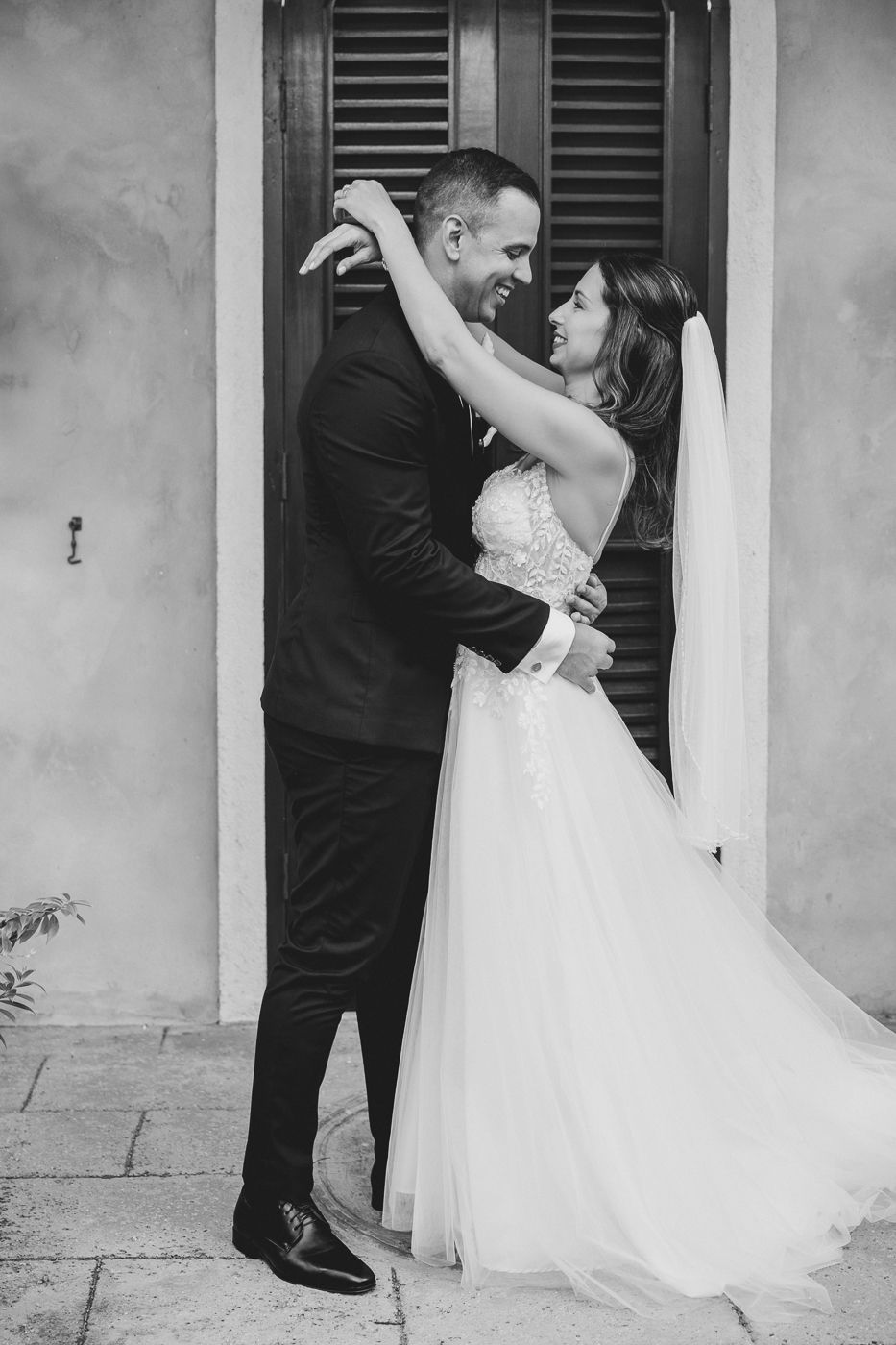 Black and white photo of a bride and groom embracing and smiling at each other on their wedding day.