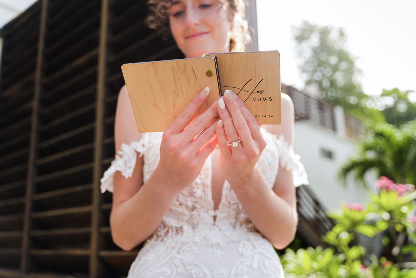 A wedding dress with delicate lace details is held up against a bright outdoor setting.