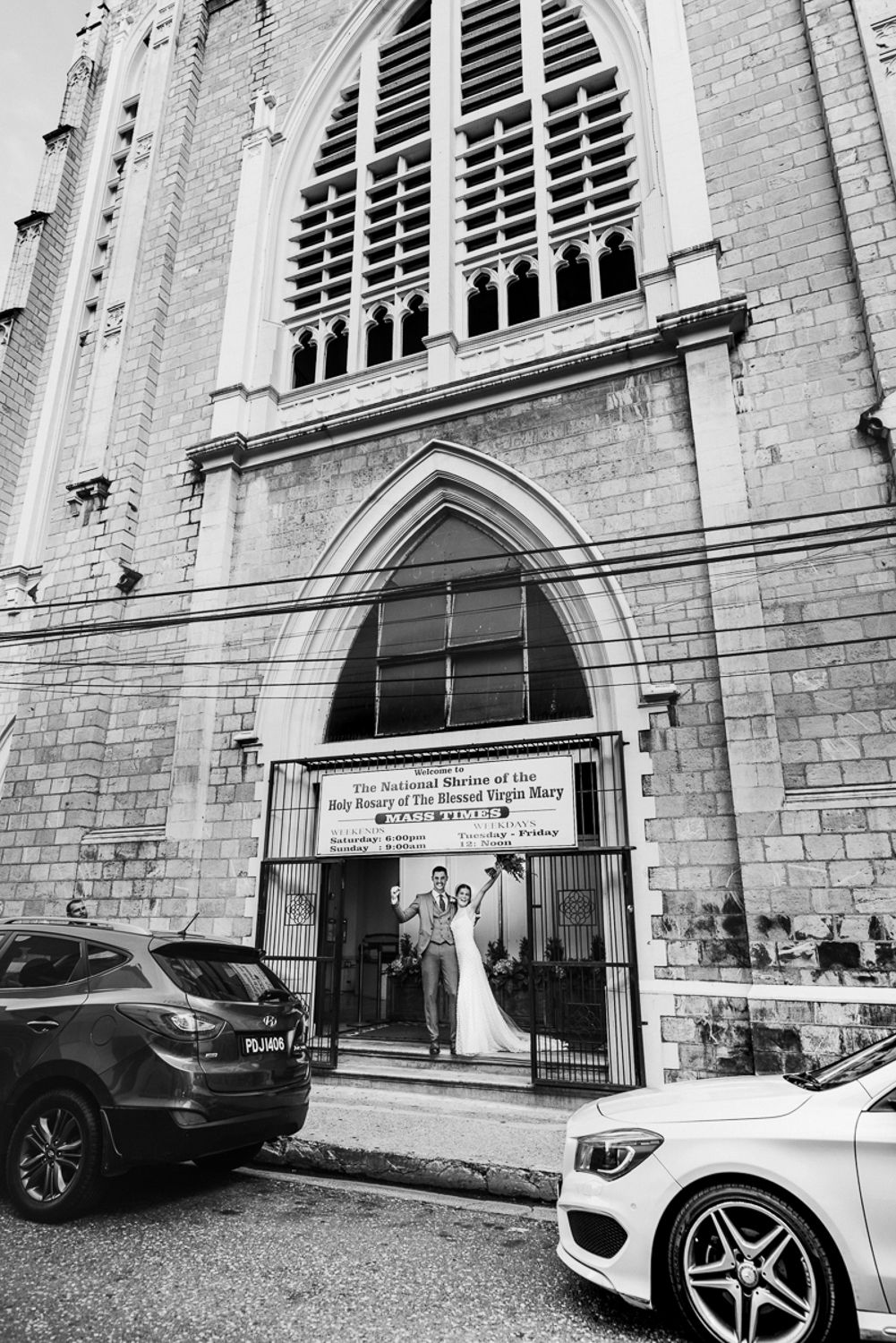Modern luxury cars parked in front of historic Gothic church facade with ornate arched windows and stonework details.