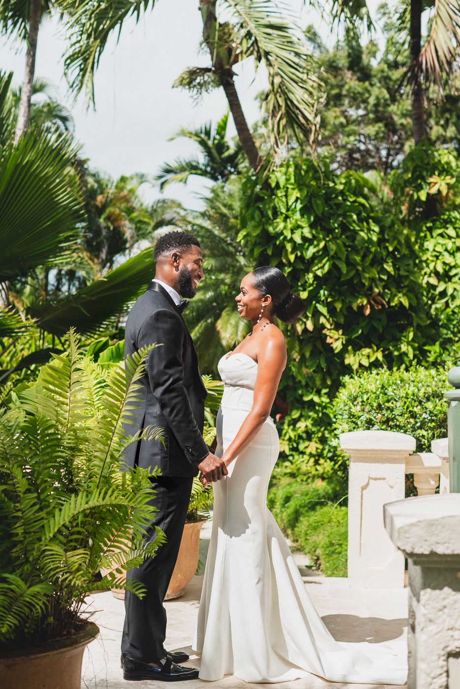 Romantic wedding portrait in a lush tropical garden setting with palm trees and white balustrades.