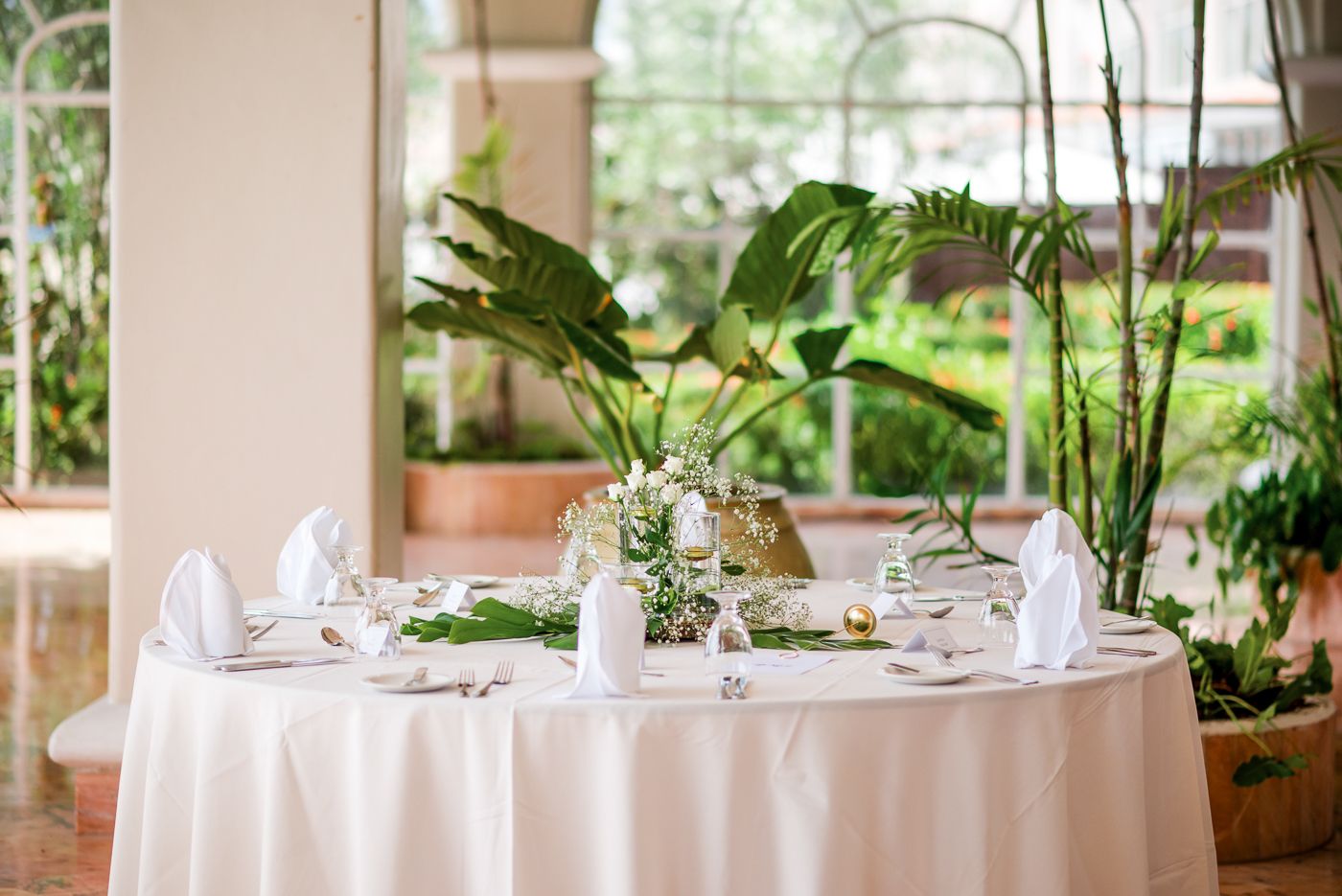 Elegant round dining table with tropical centerpiece and white linens in a garden setting.