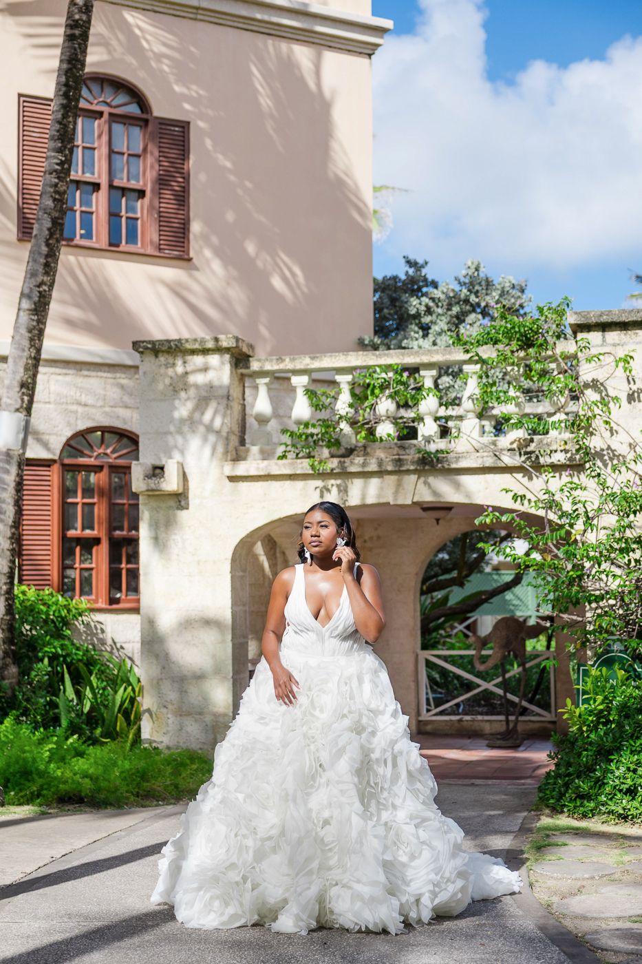 Bride in a voluminous white ruffled ball gown posing outdoors near an elegant historic building with balcony.