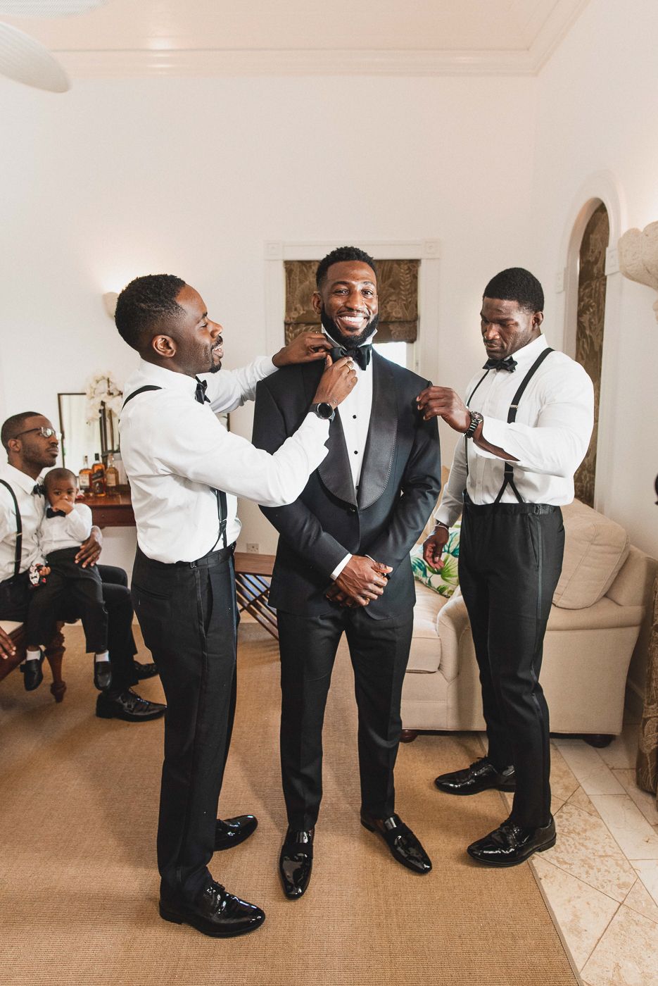 Wedding party members help groom with final adjustments to his formal attire.
