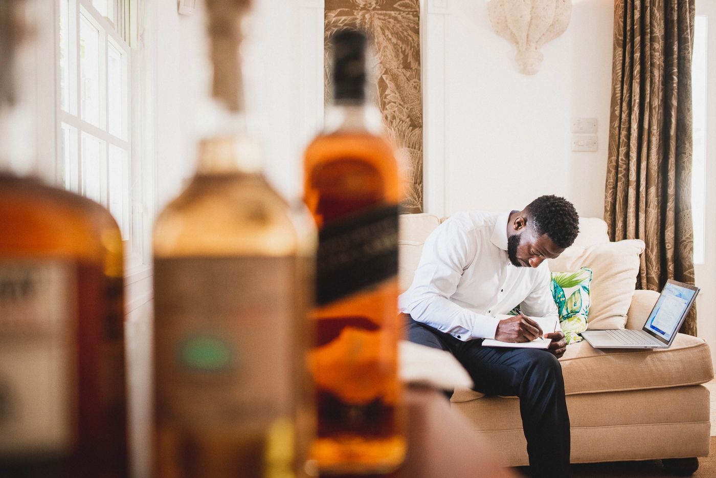 Bottles of whiskey in foreground with someone relaxing on couch in background.