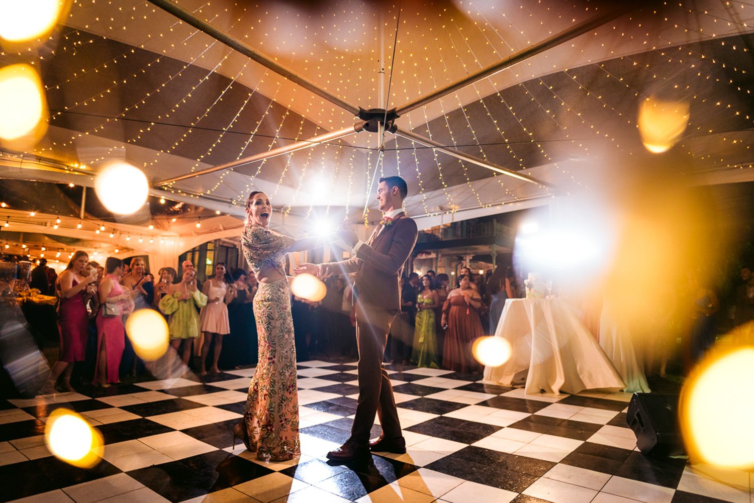 First dance of the newlyweds on a black and white checkered dance floor at a warmly lit wedding reception.