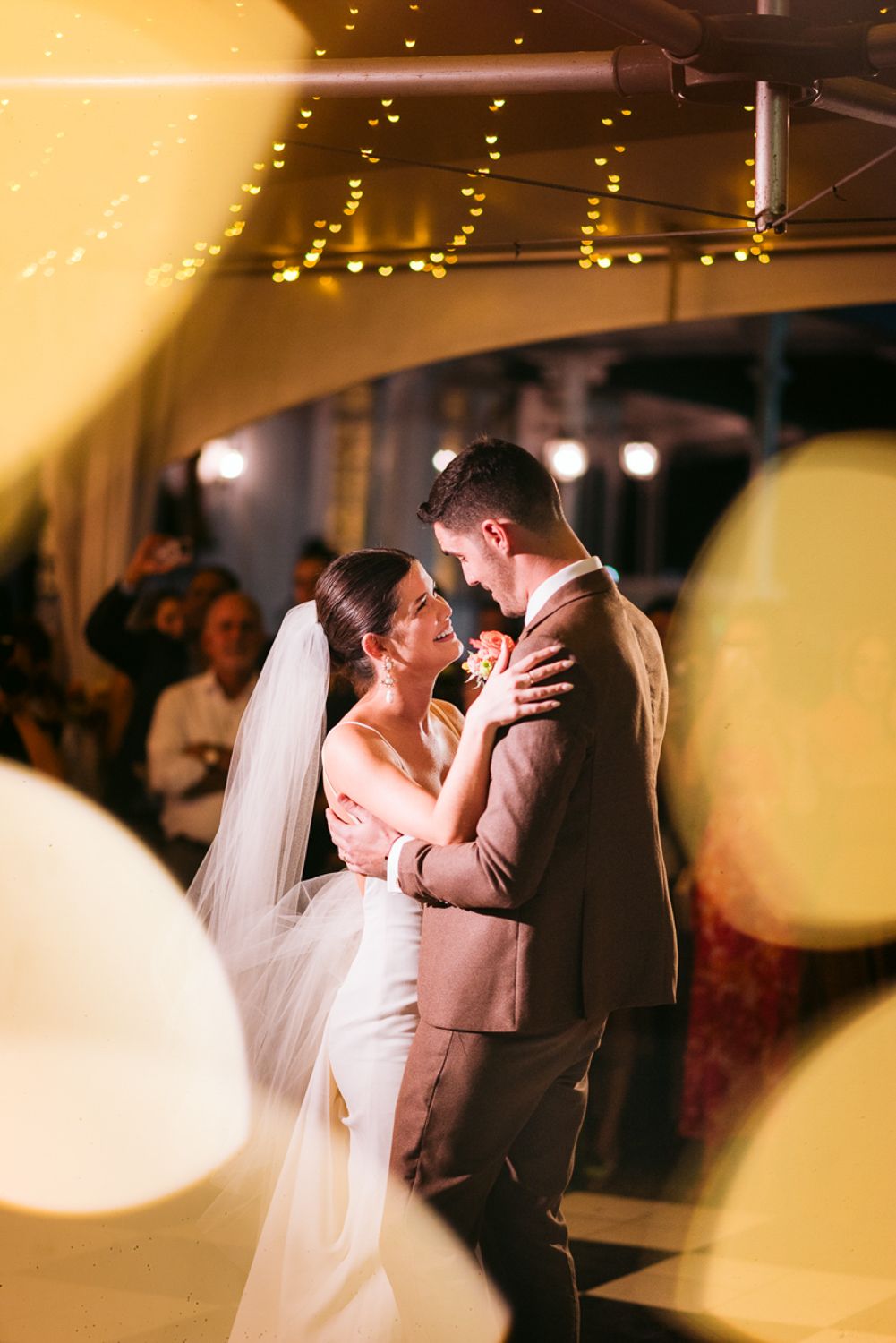 A newly married couple shares their first dance under romantic string lights and glowing bokeh effects.