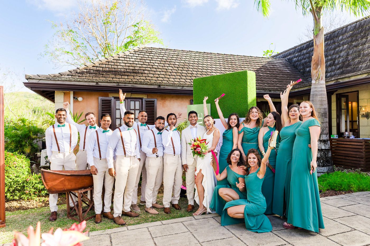 Wedding party poses in coordinated outfits of white and turquoise against tropical garden backdrop.