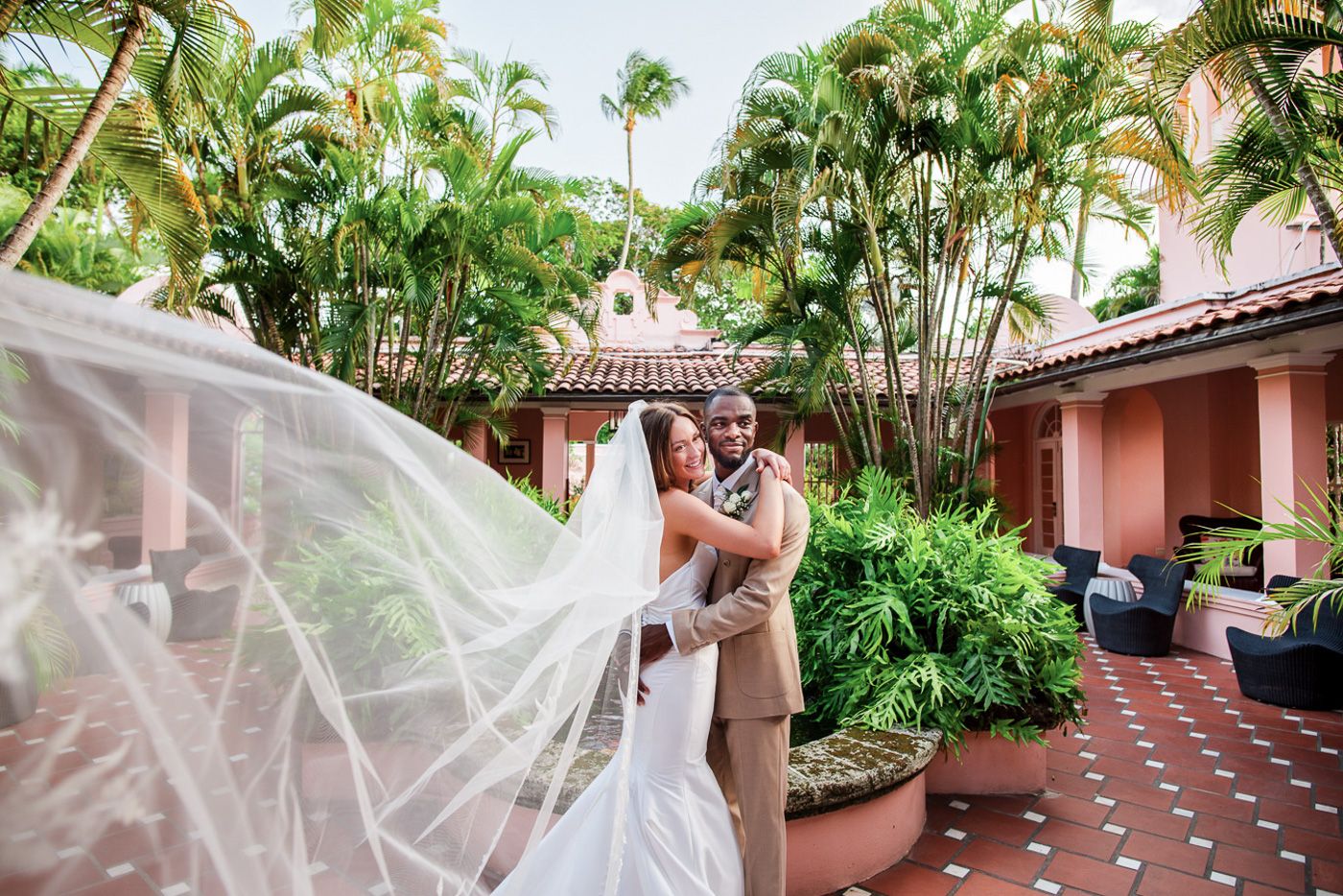Tropical garden wedding scene with flowing veil and palm trees.