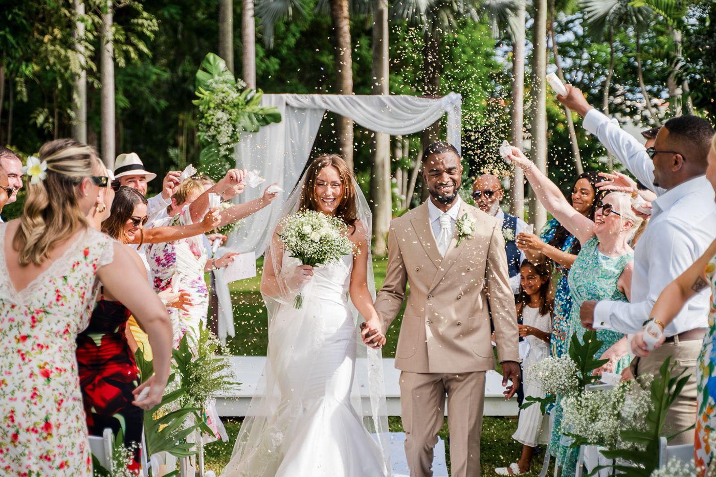 Wedding party and guests sharing joyful moments during an outdoor tropical garden celebration.