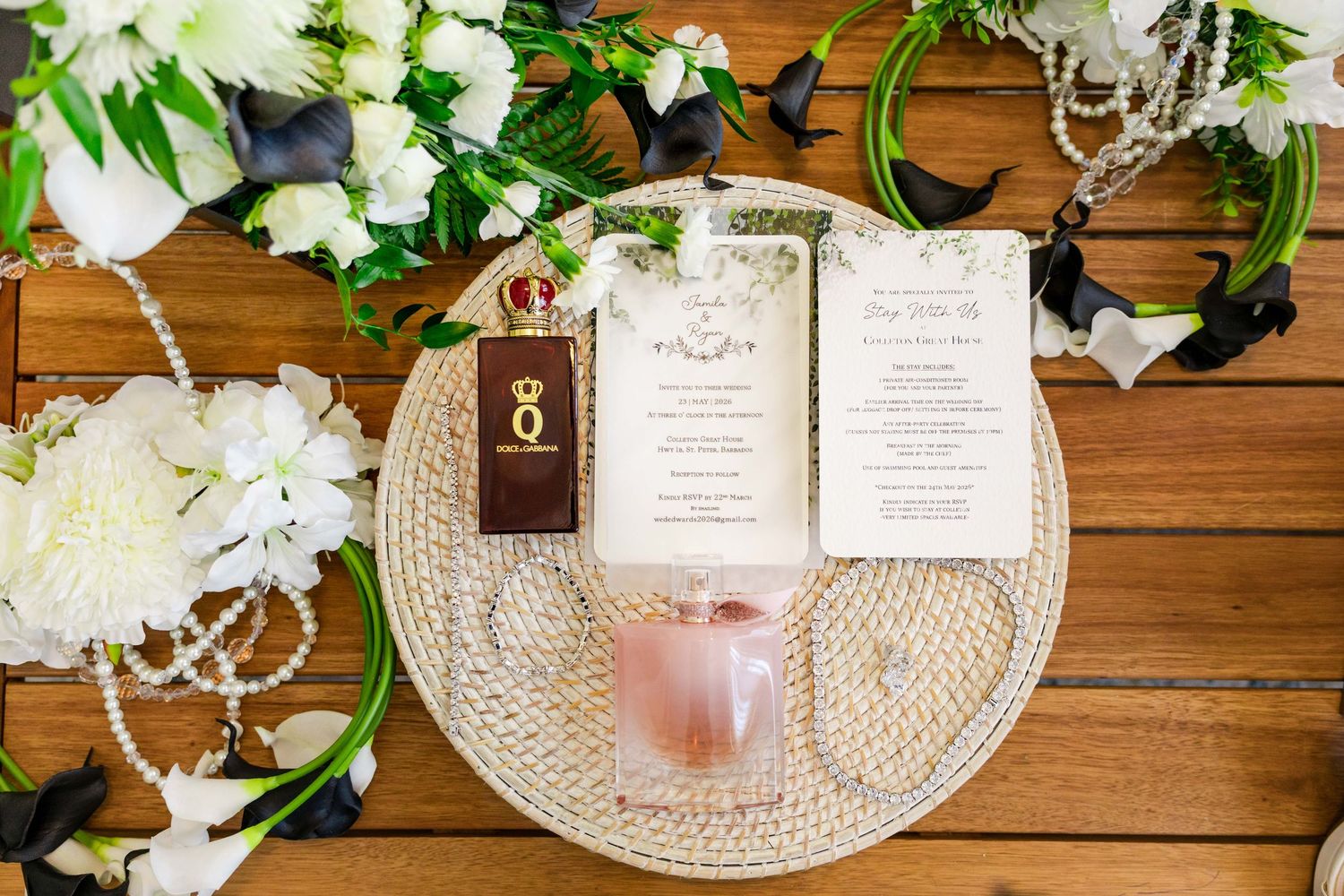 Elegant wedding flat lay with floral arrangements, menu cards, ring box, and pearl necklace on wooden table.