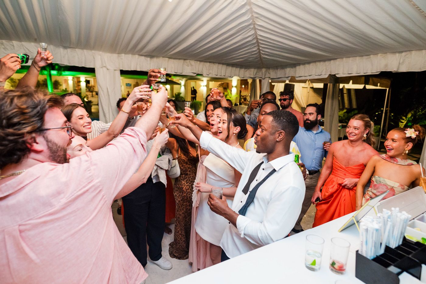 Wedding celebration with guests dancing under a white tent during an evening reception.