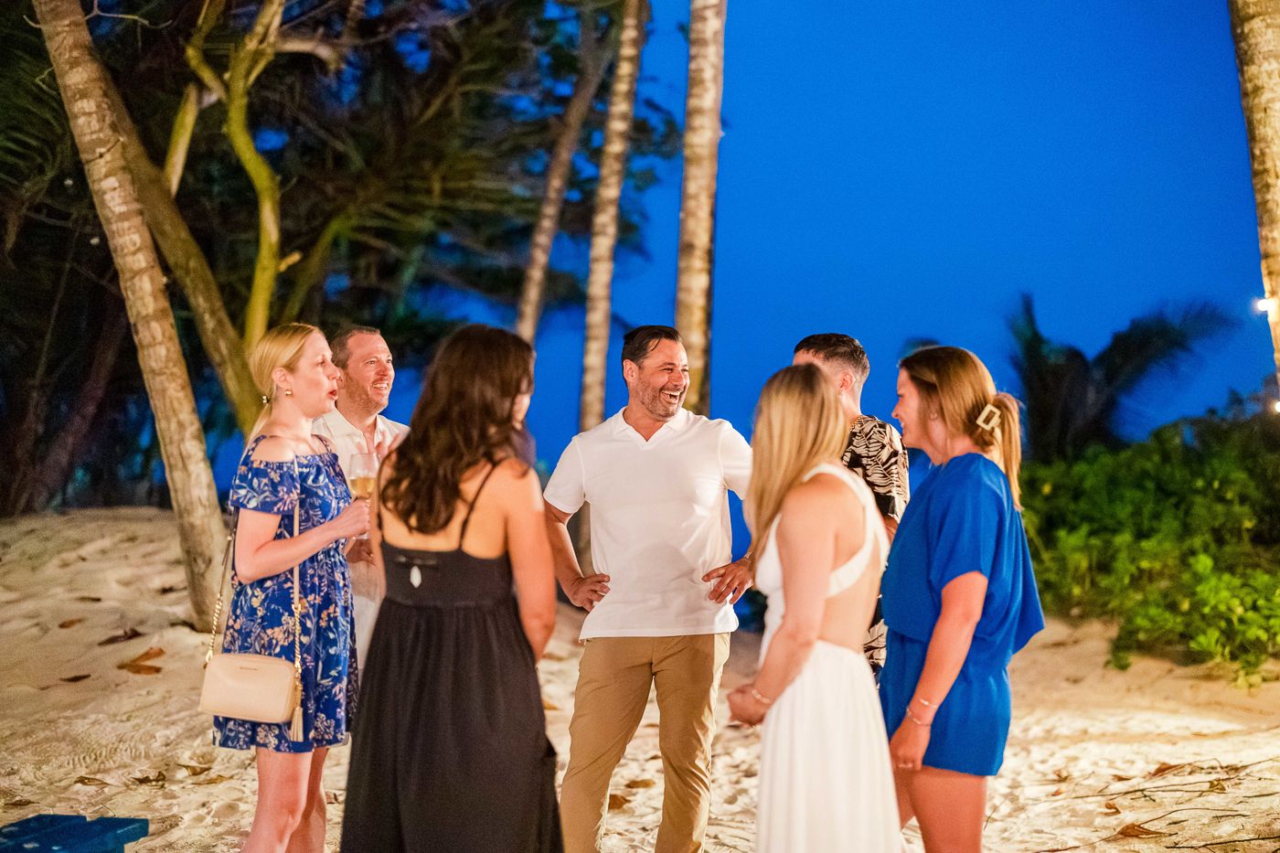 Group of friends celebrating on a tropical beach at night surrounded by palm trees.