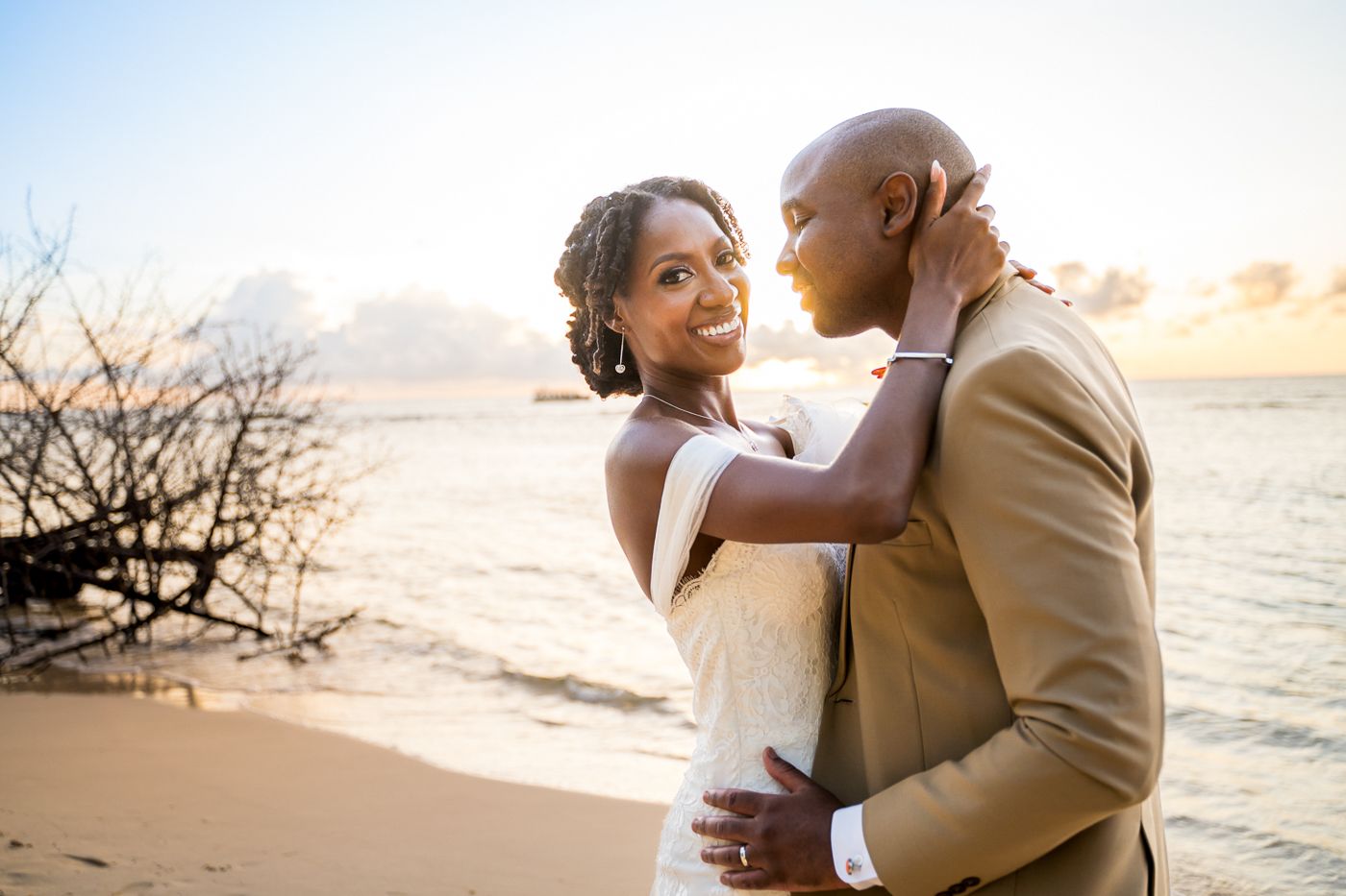 Happy couple embraces on sandy beach at golden sunset during tropical destination wedding.