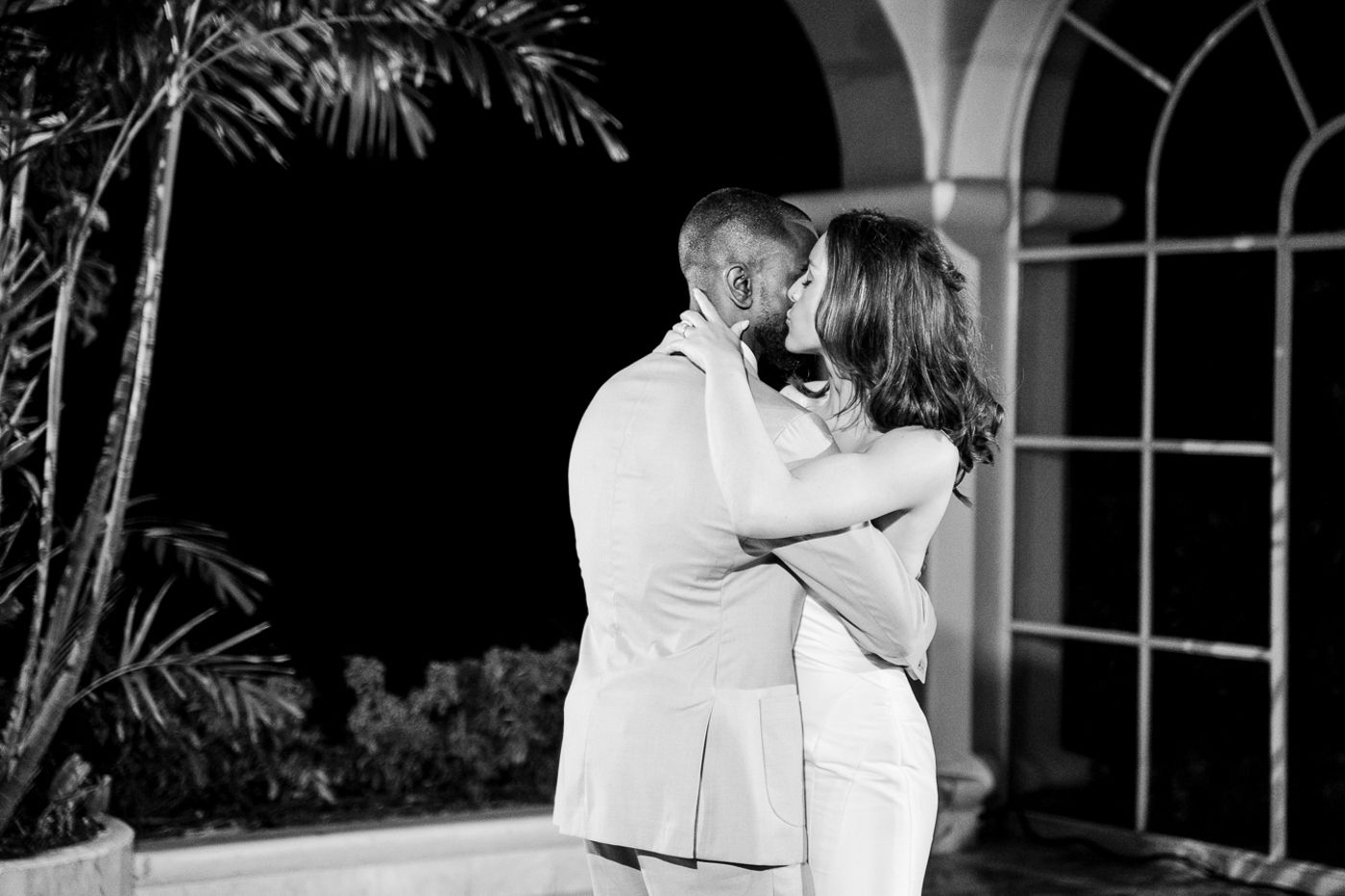 A romantic black and white photo of a couple embracing under an arched walkway at night.