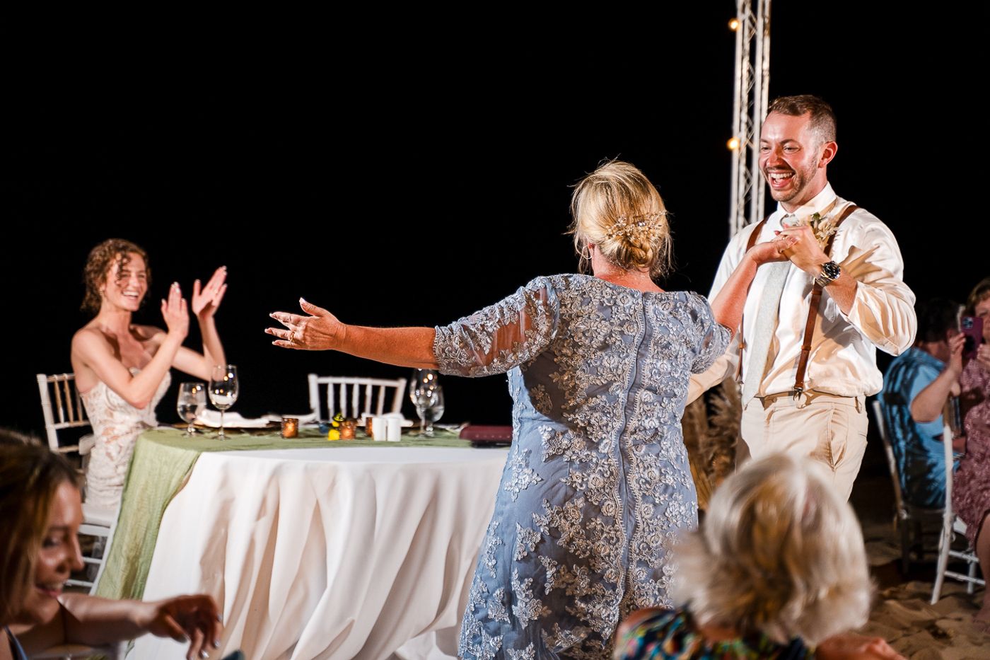 Beachside reception tables decorated with white linens and string lights create a romantic evening atmosphere.