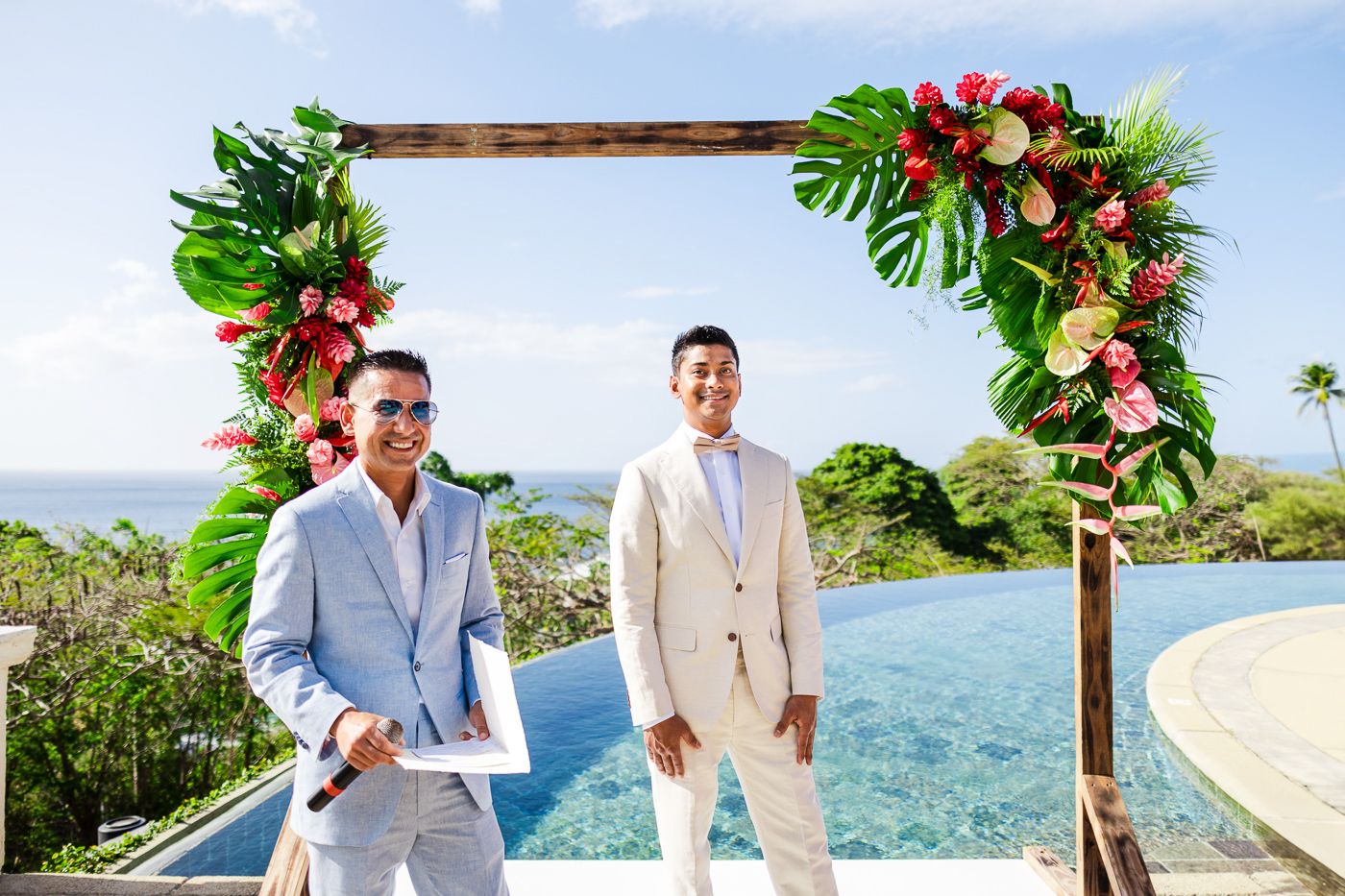 Wedding arch decorated with tropical flowers and greenery frames ocean view ceremony setup.